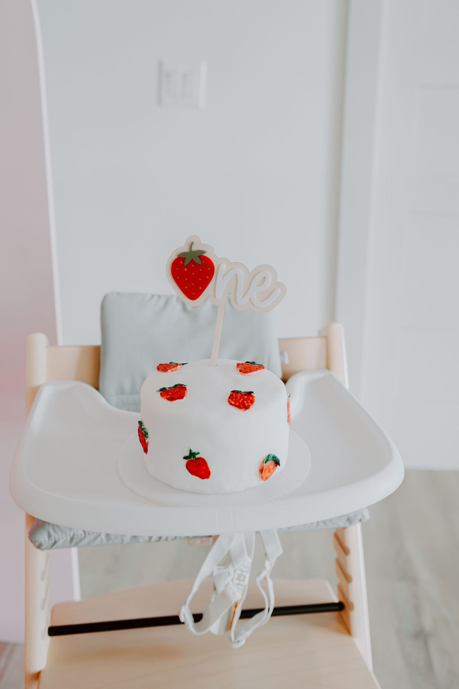 White high chair decorated with cute strawberry patterns and a heart-shaped topper for a birthday celebration.