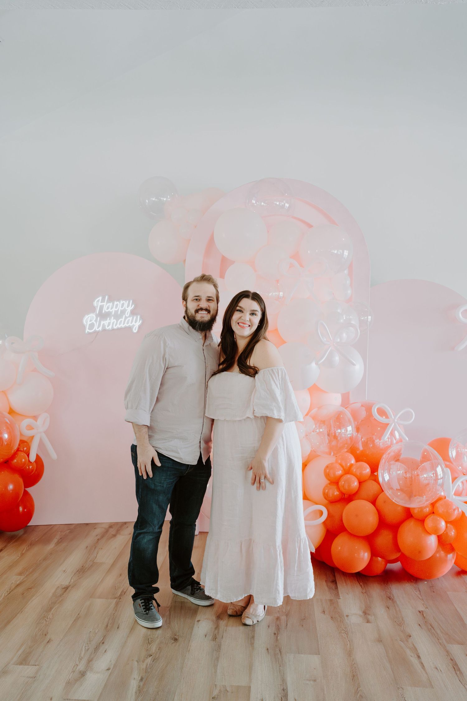 Couple posing in front of elegant pink and coral balloon installation at celebration.