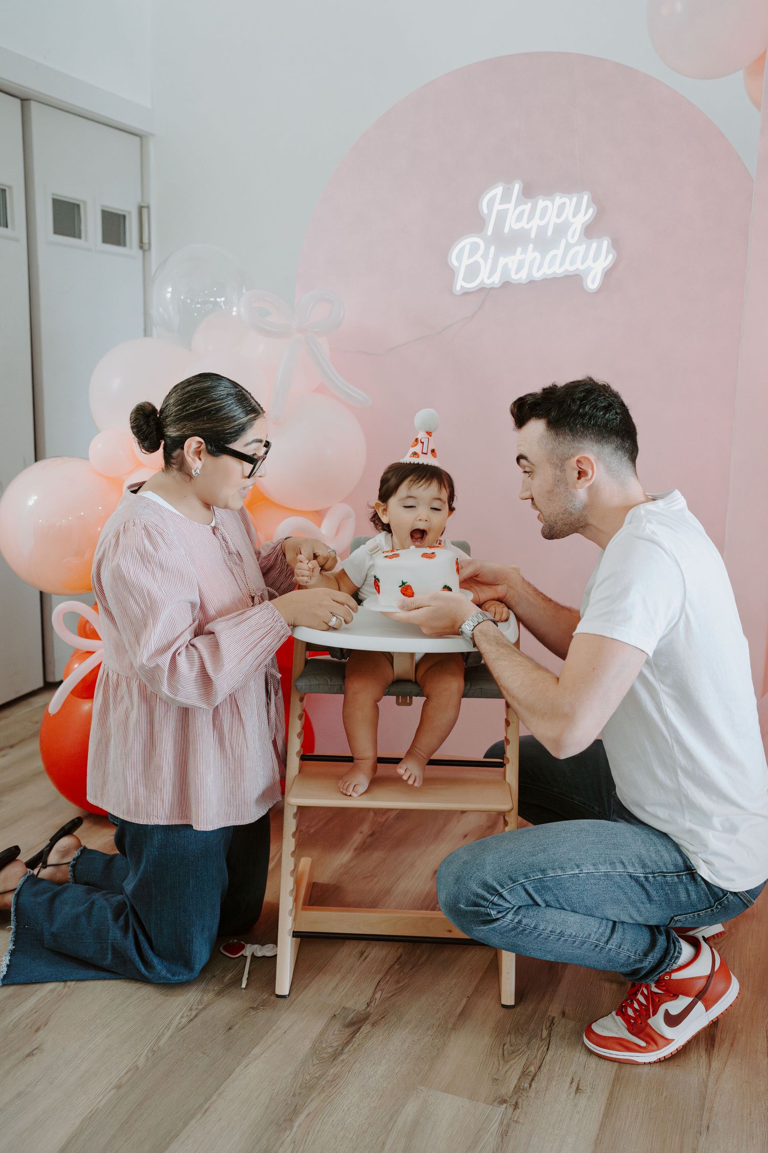 Intimate family moment during baby's birthday party with pink balloon decorations.
