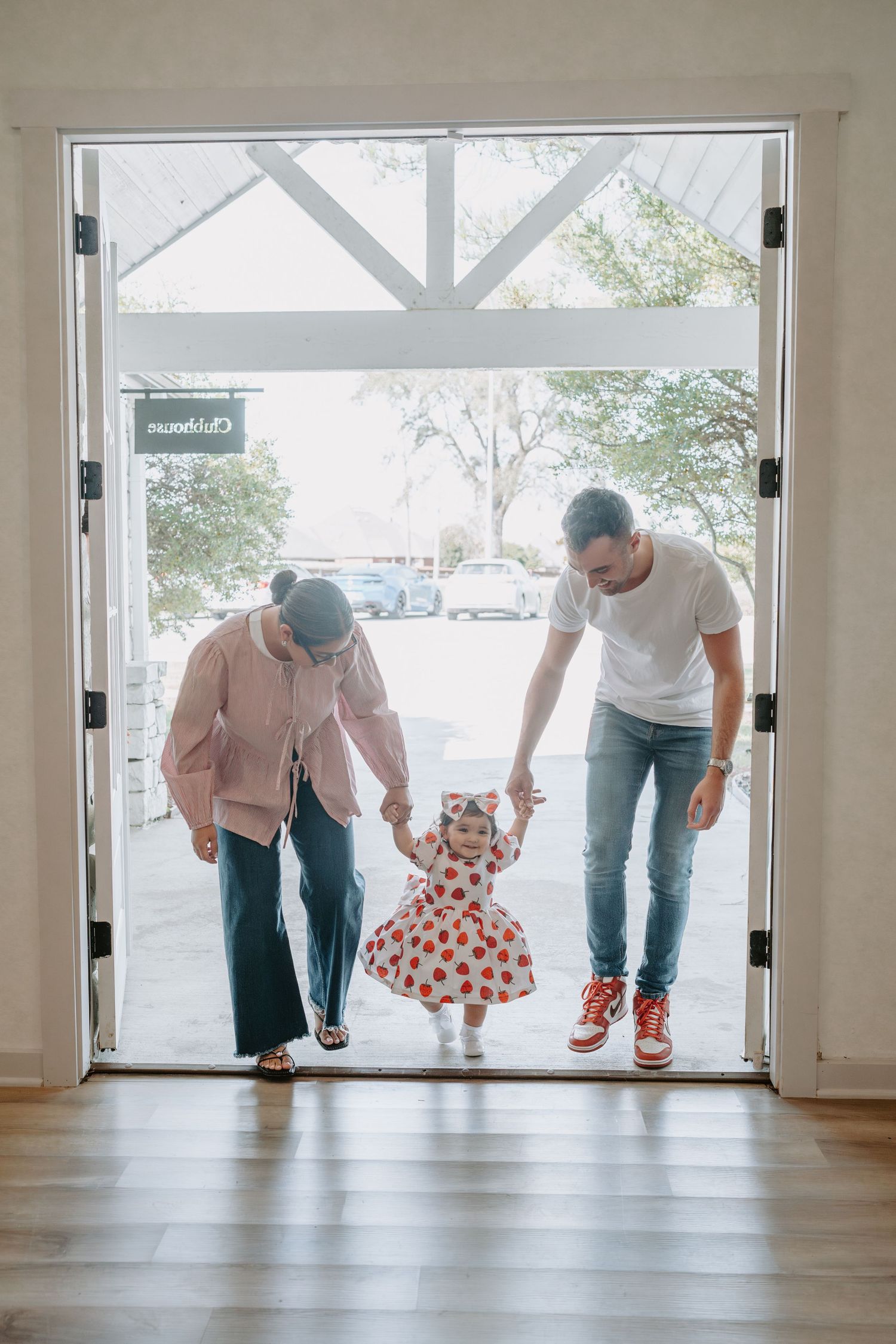 Family members bend down playfully in a bright room with hardwood floors and large windows.