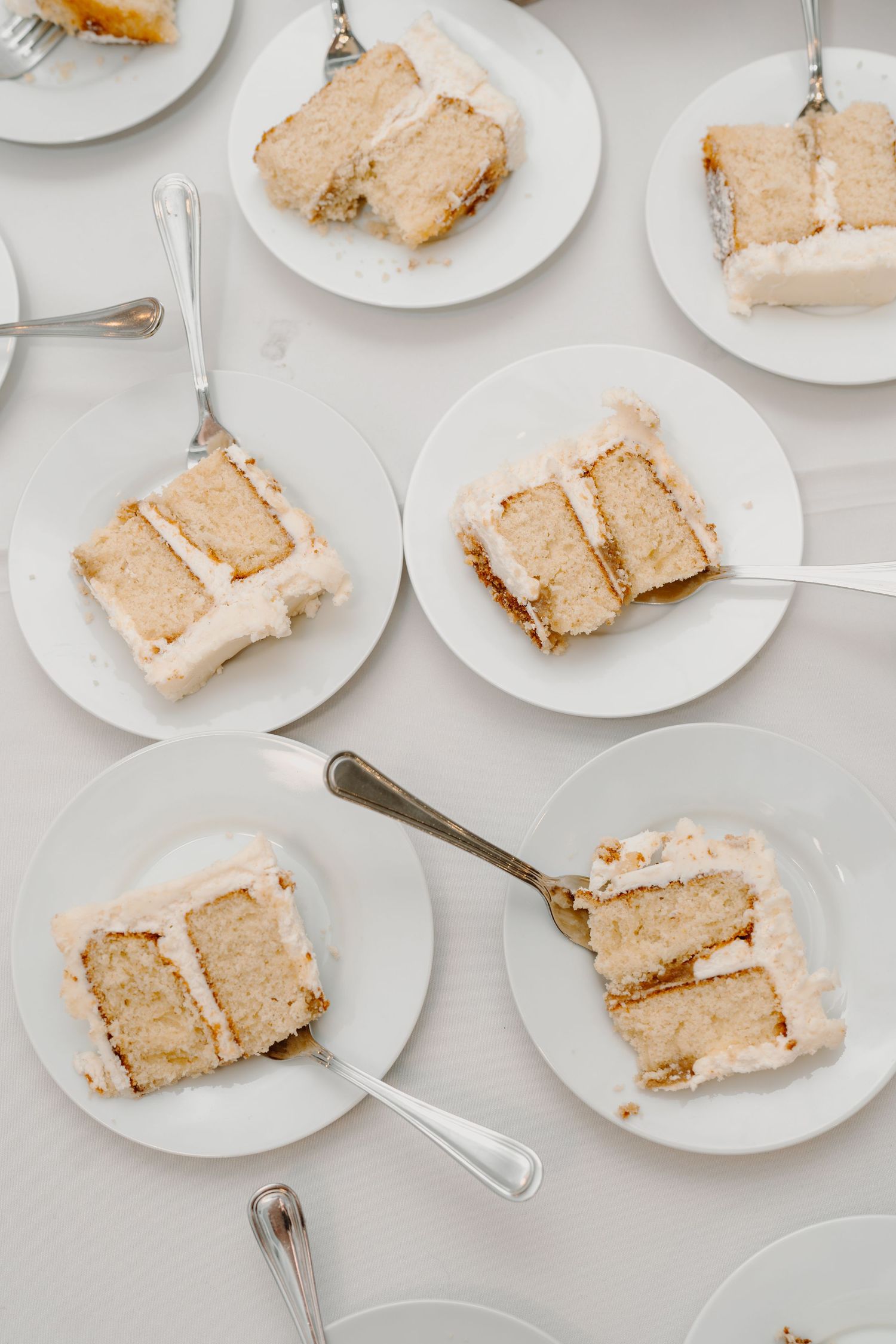 Multiple plates of sliced wedding cake arranged on a white tablecloth.