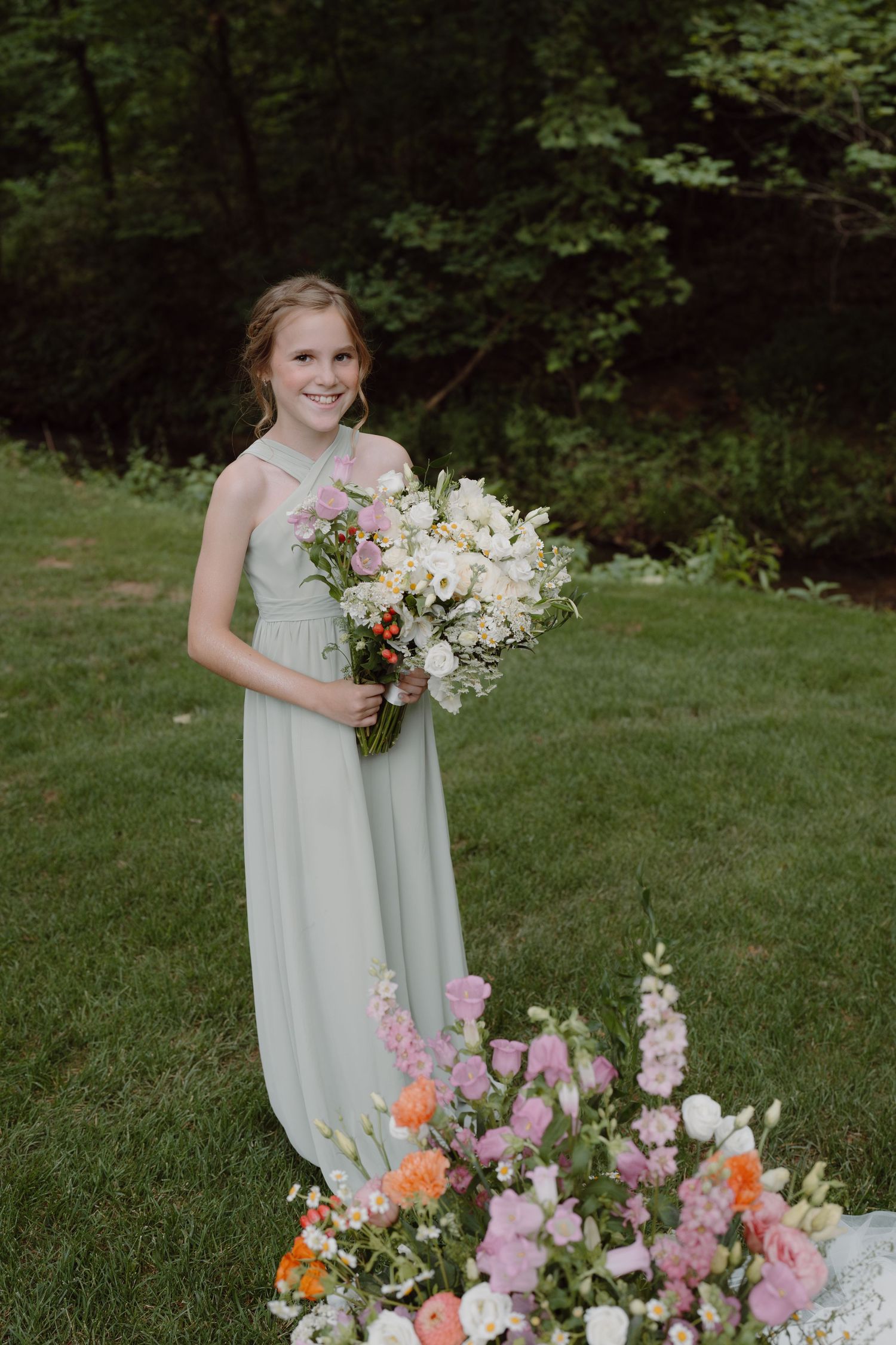 Bridesmaid in pale mint dress poses with vibrant pink and orange floral arrangements outdoors.