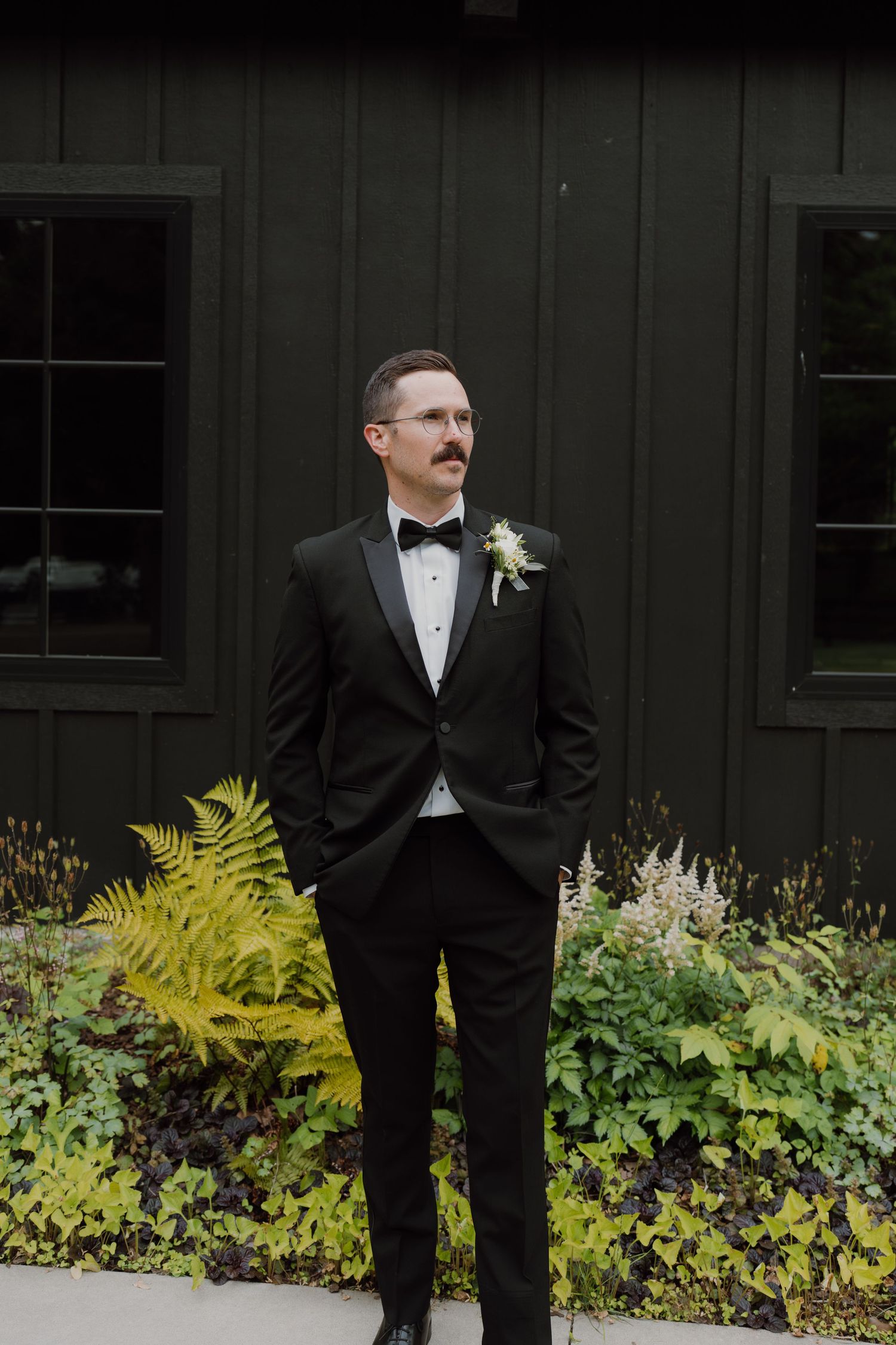 A formal portrait showing someone in a black bow tie and tuxedo against a dark building exterior.