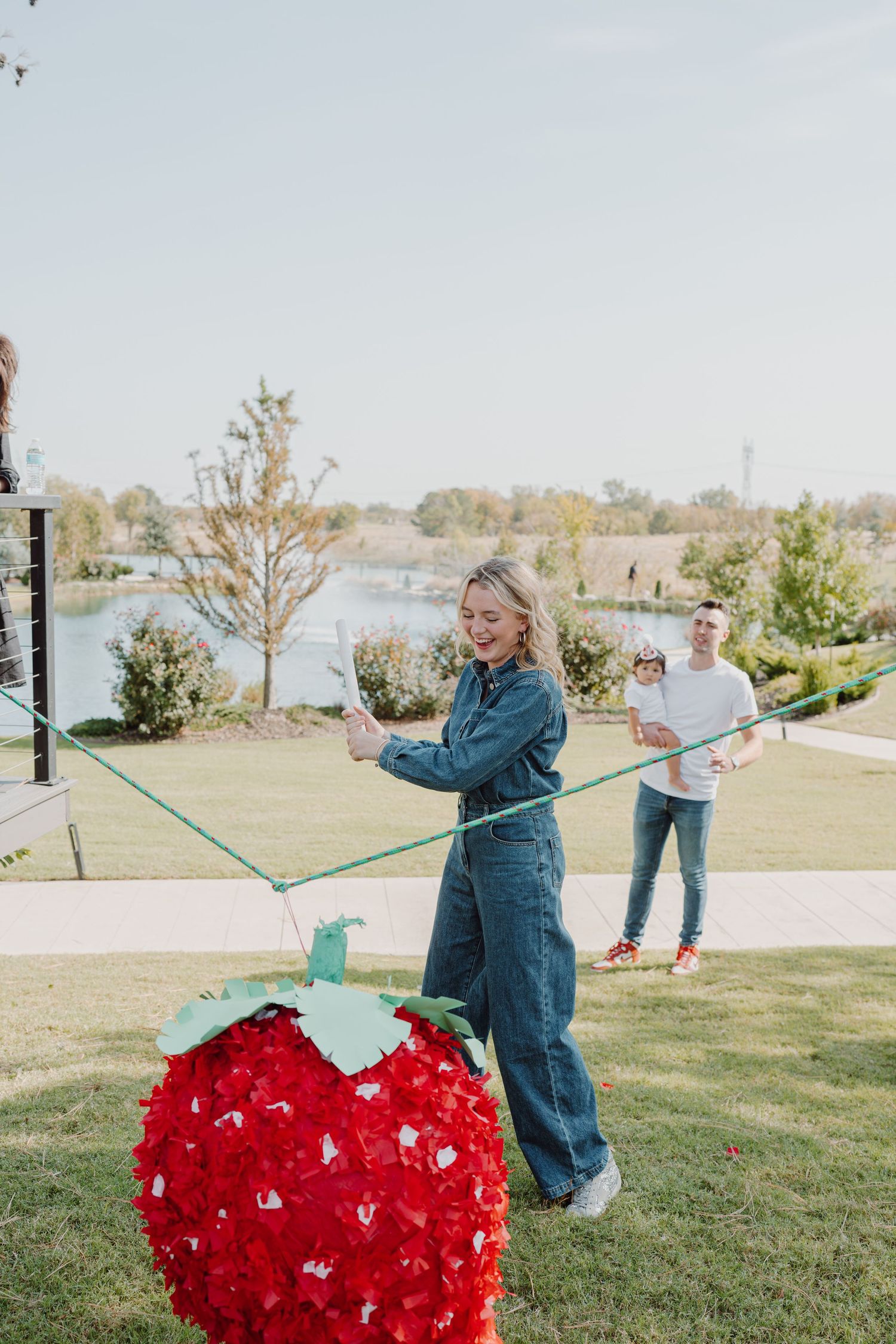 Someone swings a large red heart-shaped piñata on a string in a park setting.