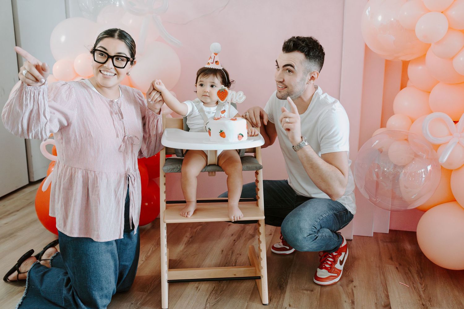 Birthday celebration setup with pink balloon decorations and white high chair.