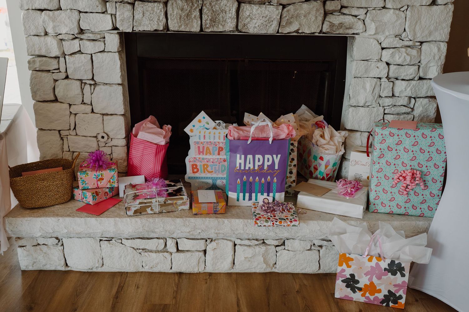 Colorful birthday gift bags and presents arranged on a stone fireplace ledge with decorative elements.