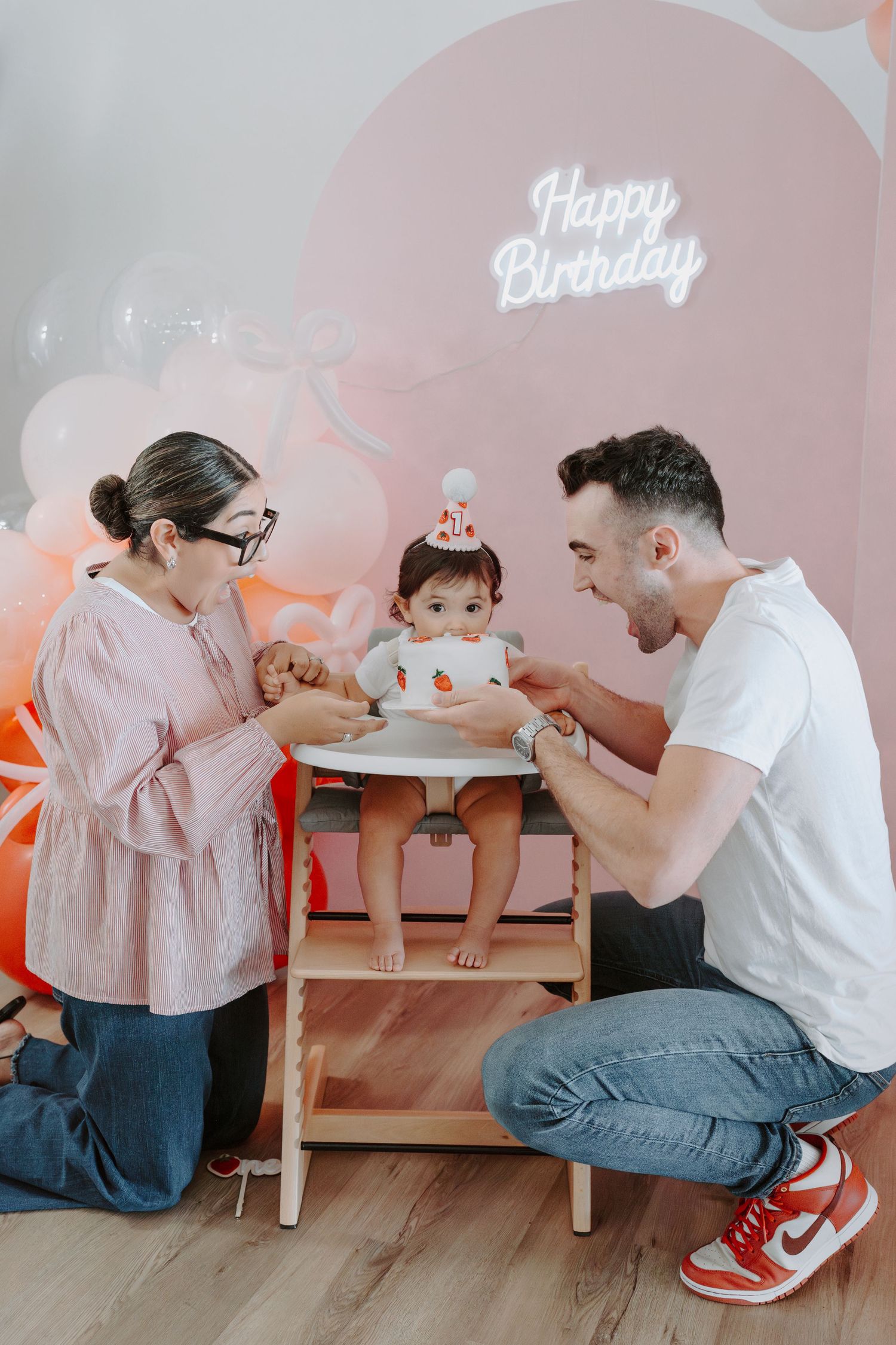Birthday celebration with cake and pink balloon decorations against pastel backdrop.