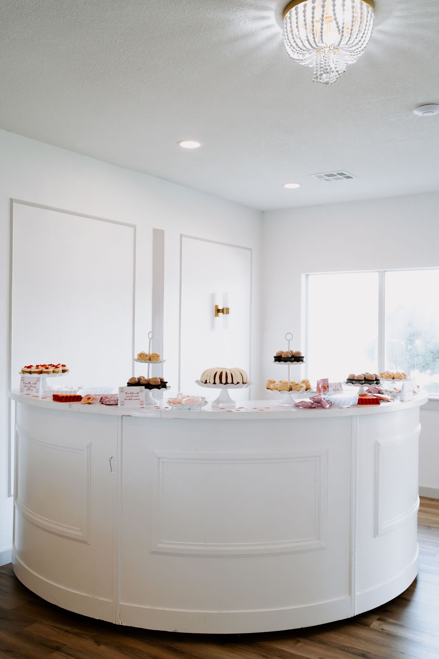 Elegant white curved wall with crystal chandelier and dessert displays in a modern event space.