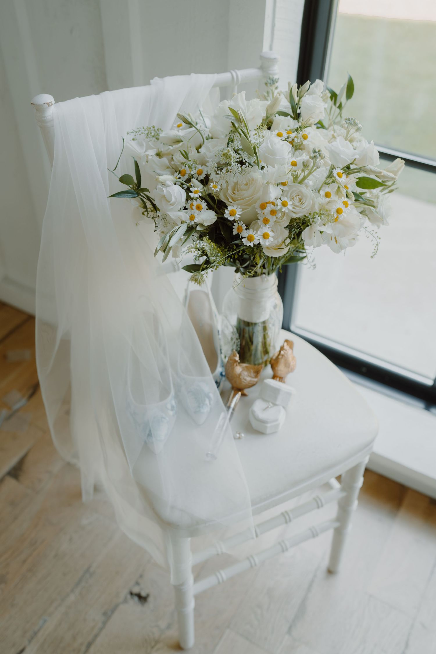 White floral arrangements with roses and daisies in glass jars on a windowsill.