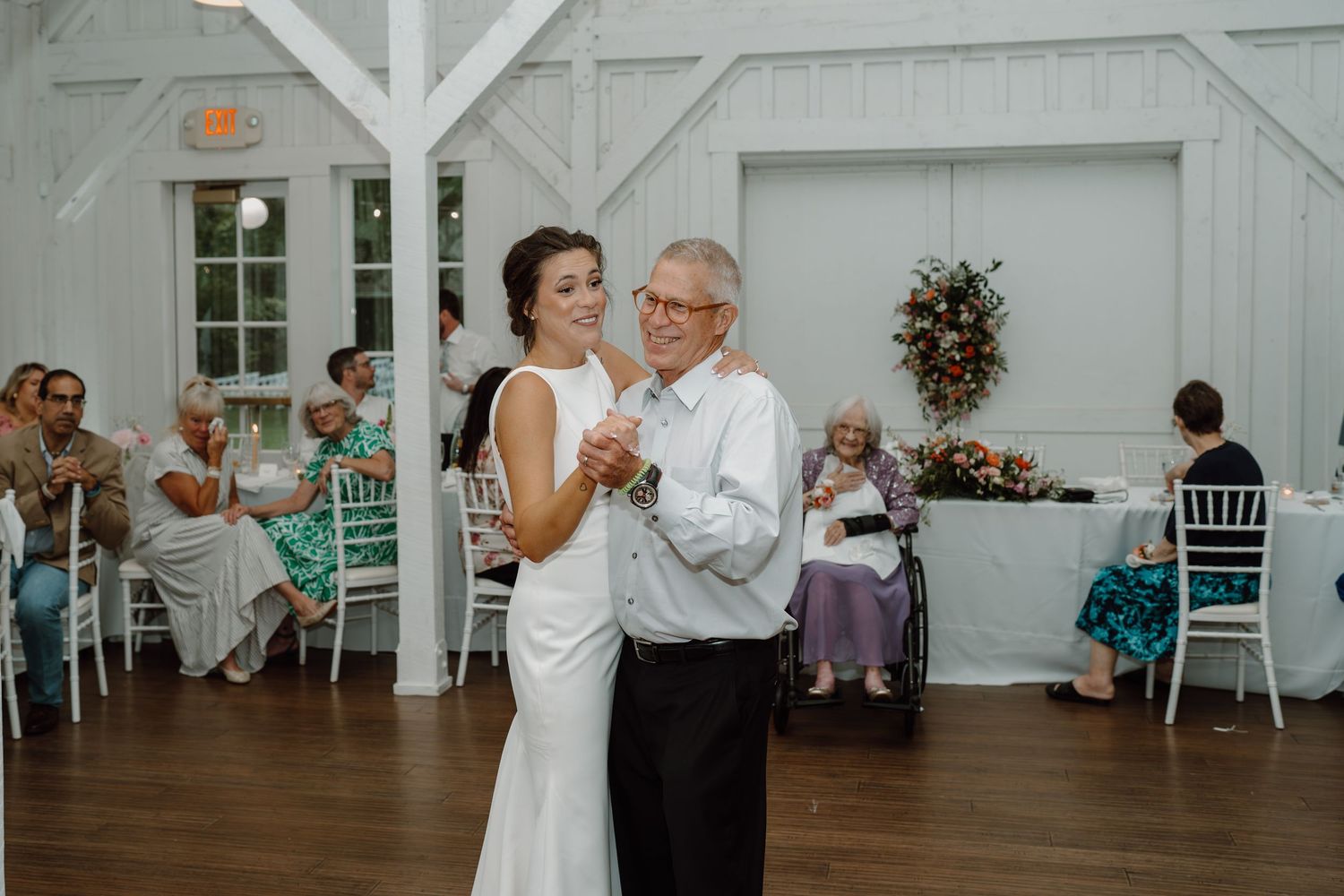 A special dance moment in an elegant white barn venue with guests watching from their tables.