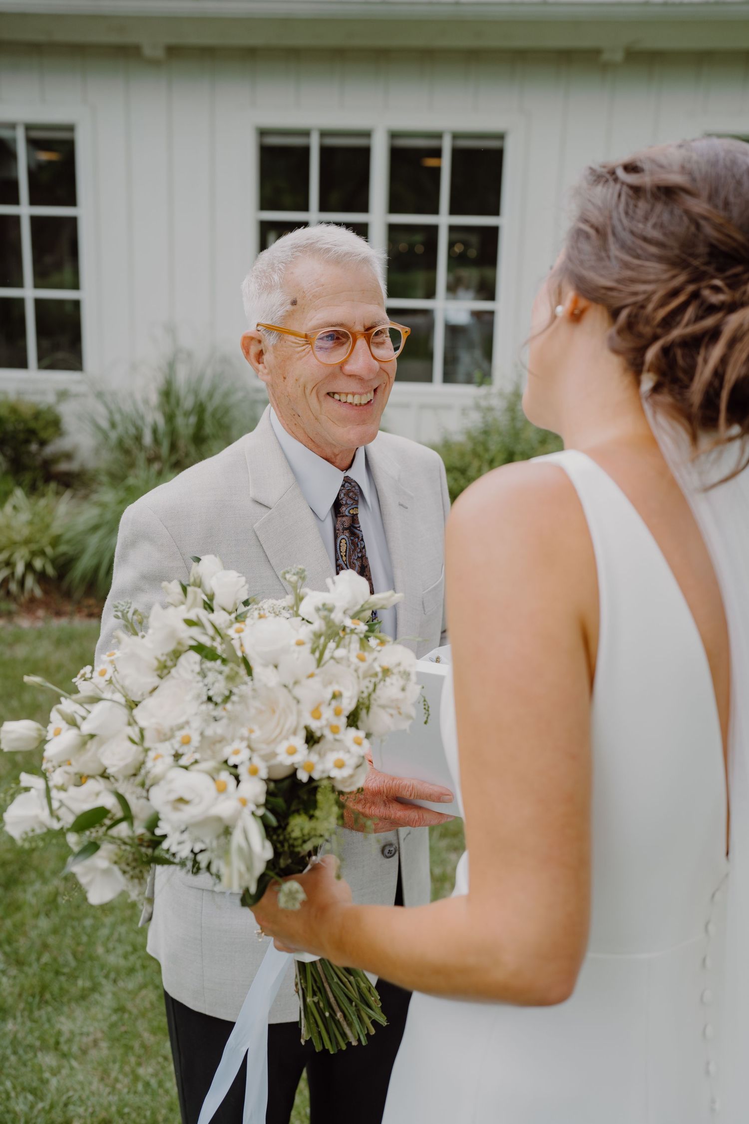 A touching moment shared between a bride and an elderly gentleman in a light suit holding a beautiful white bouquet.