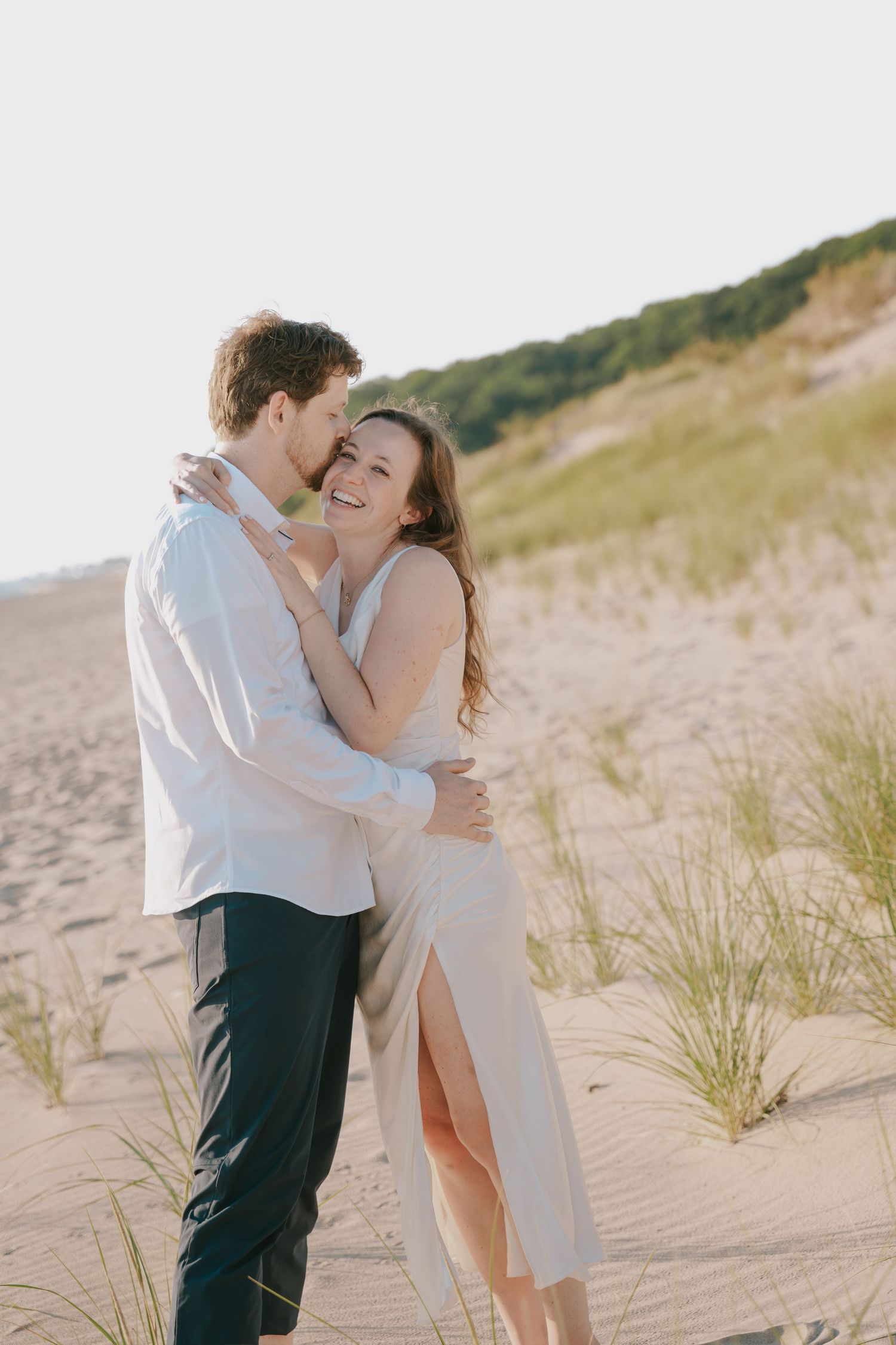 A joyful moment shared between a couple on a sandy beach with dunes.