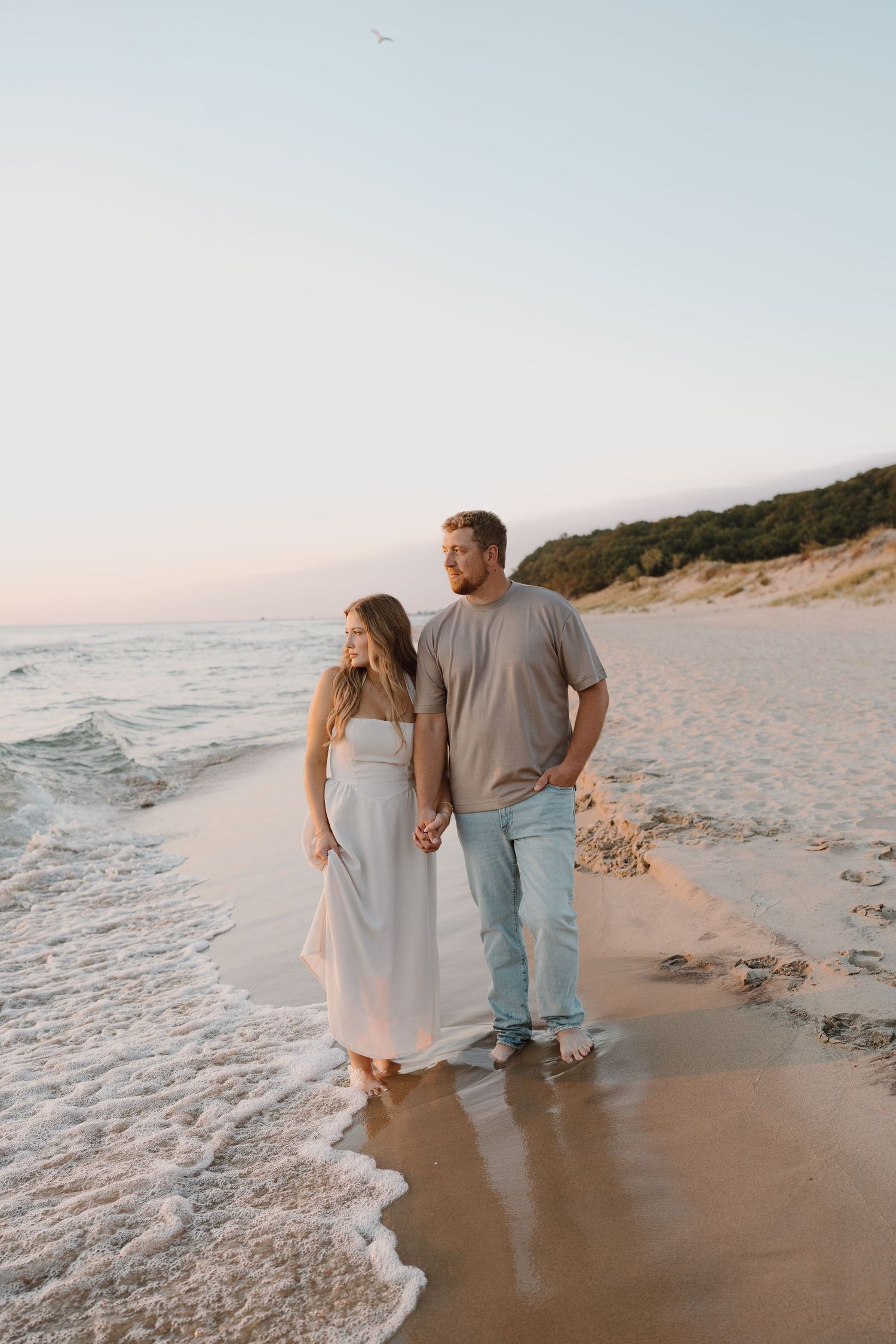 A couple shares intimate moments while walking along a scenic coastal beach at sunset.