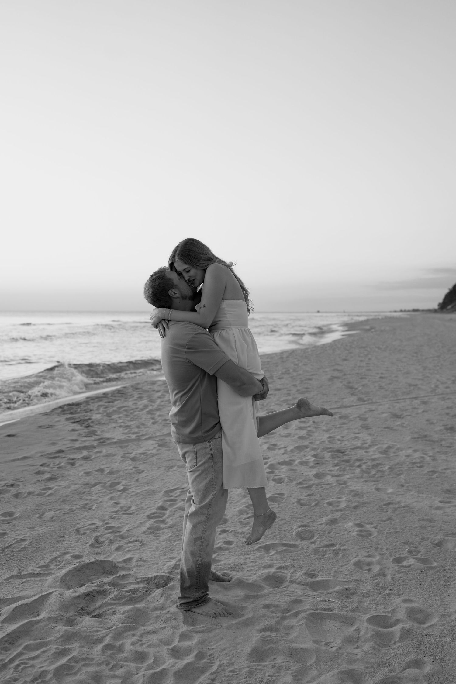 Black and white photo of a couple embracing on a peaceful beach.