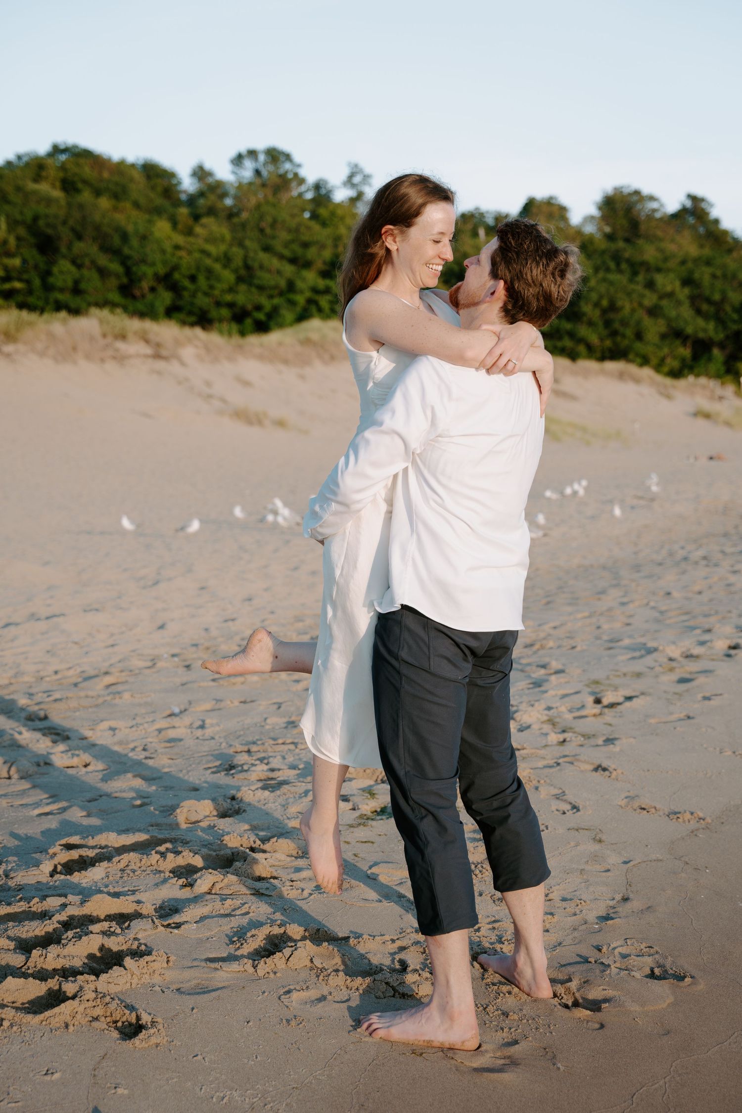 Couple in casual attire sharing intimate moments on sandy beach with seagulls.