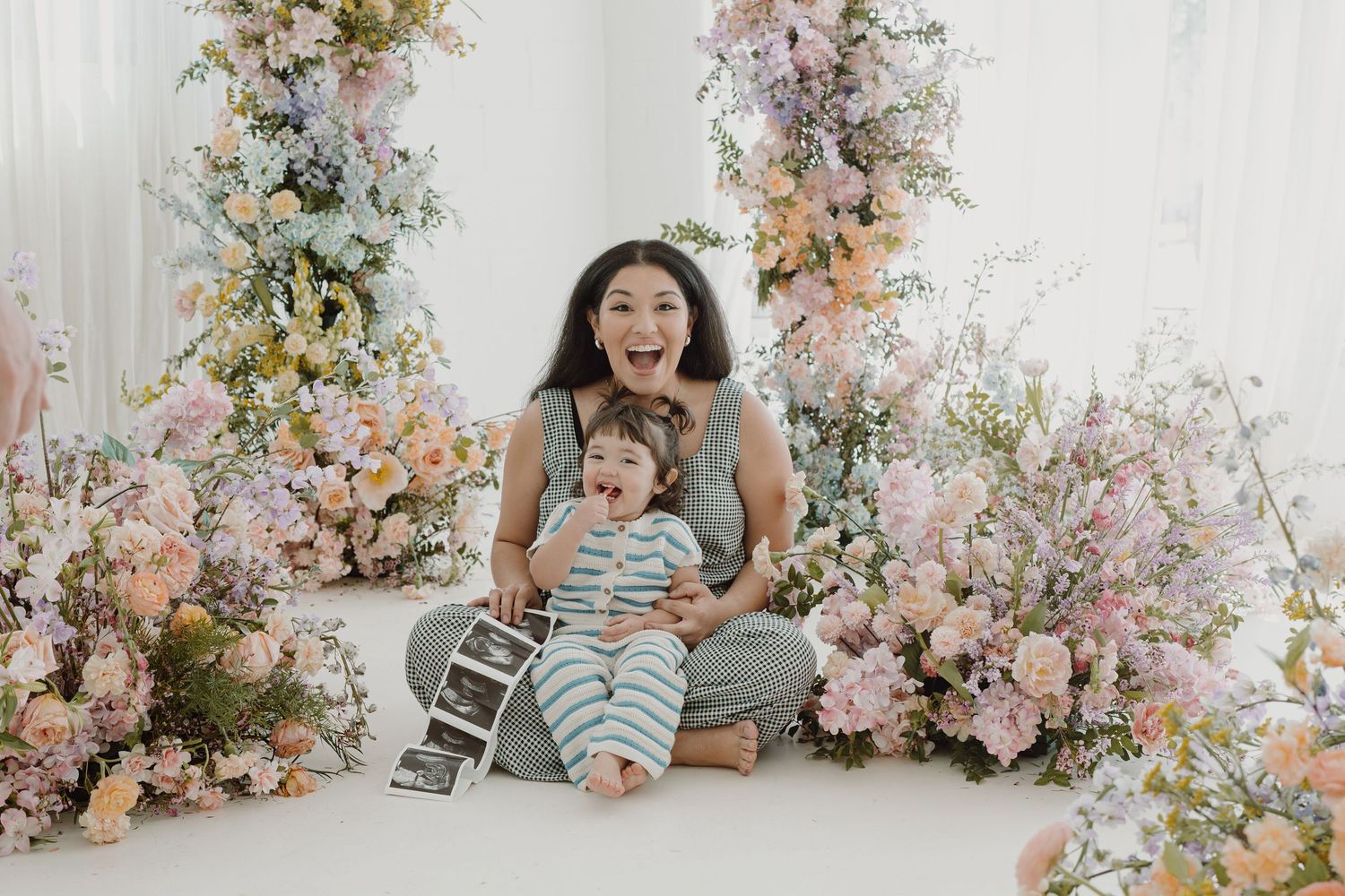 Studio portrait with elegant floral arrangements in soft pastel tones creating a dreamy backdrop.
