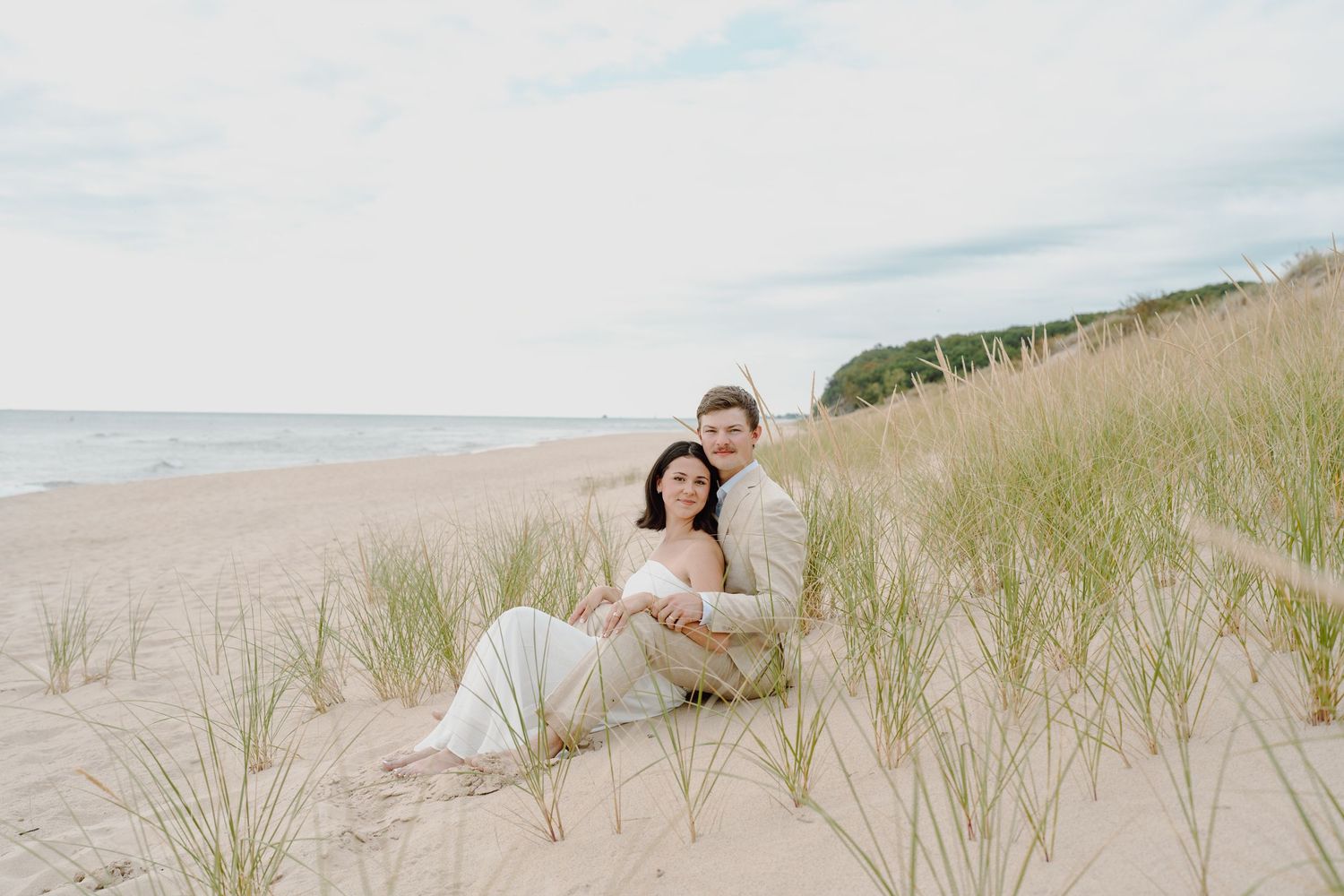 Wide angle view of couple relaxing on beach dunes with ocean in background.