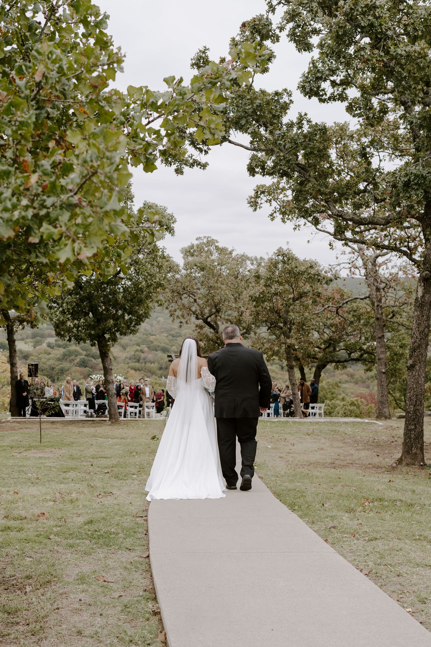 Wedding couple walking down curved pathway after outdoor ceremony with guests in background.