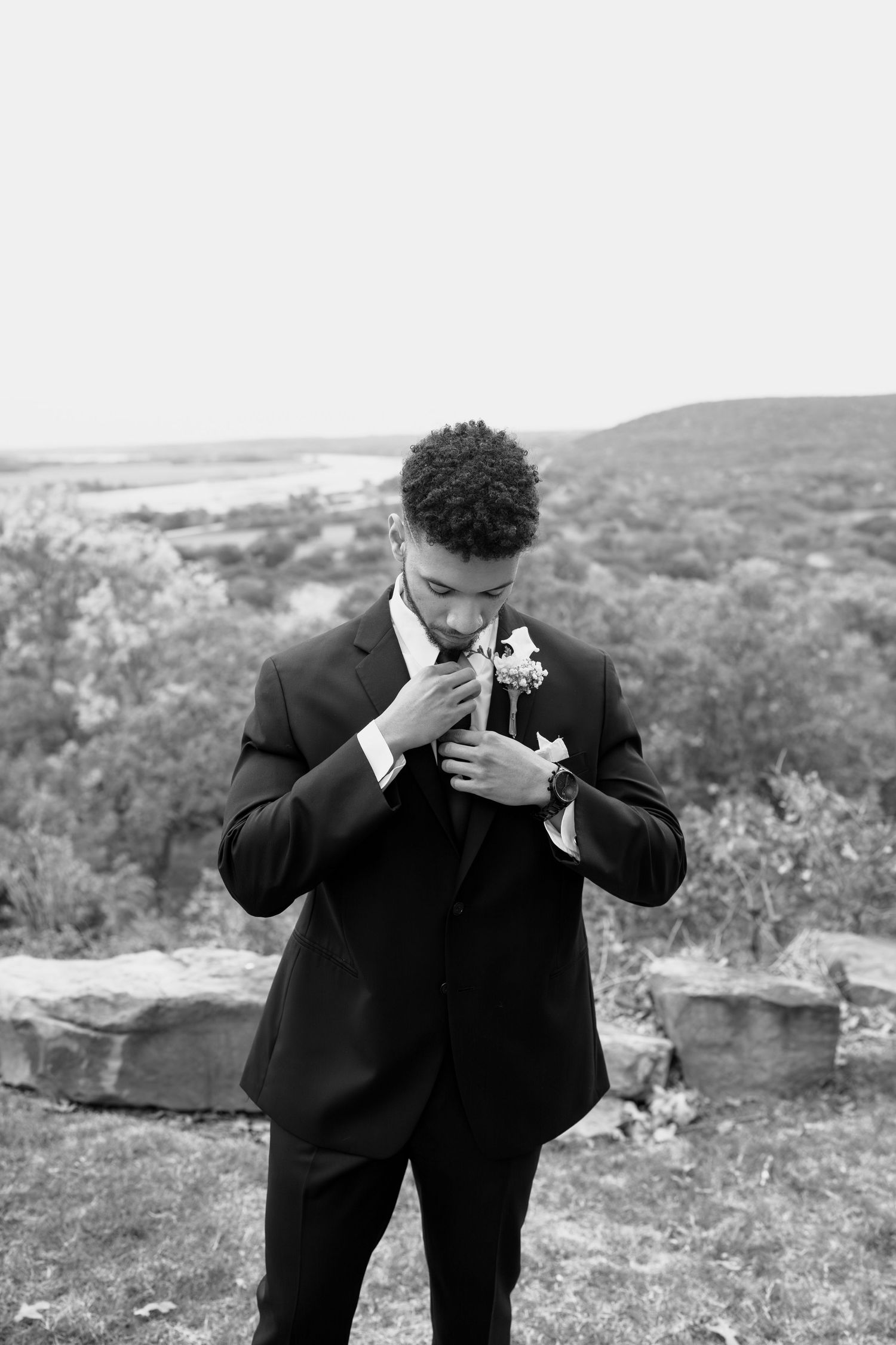 Emotional wedding moment captured as person in black suit wipes tears on scenic overlook.