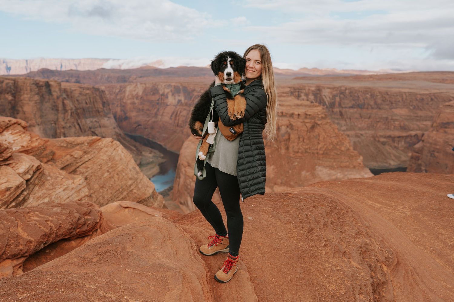 Adventure seeker poses with dog on red rock formations in desert landscape.