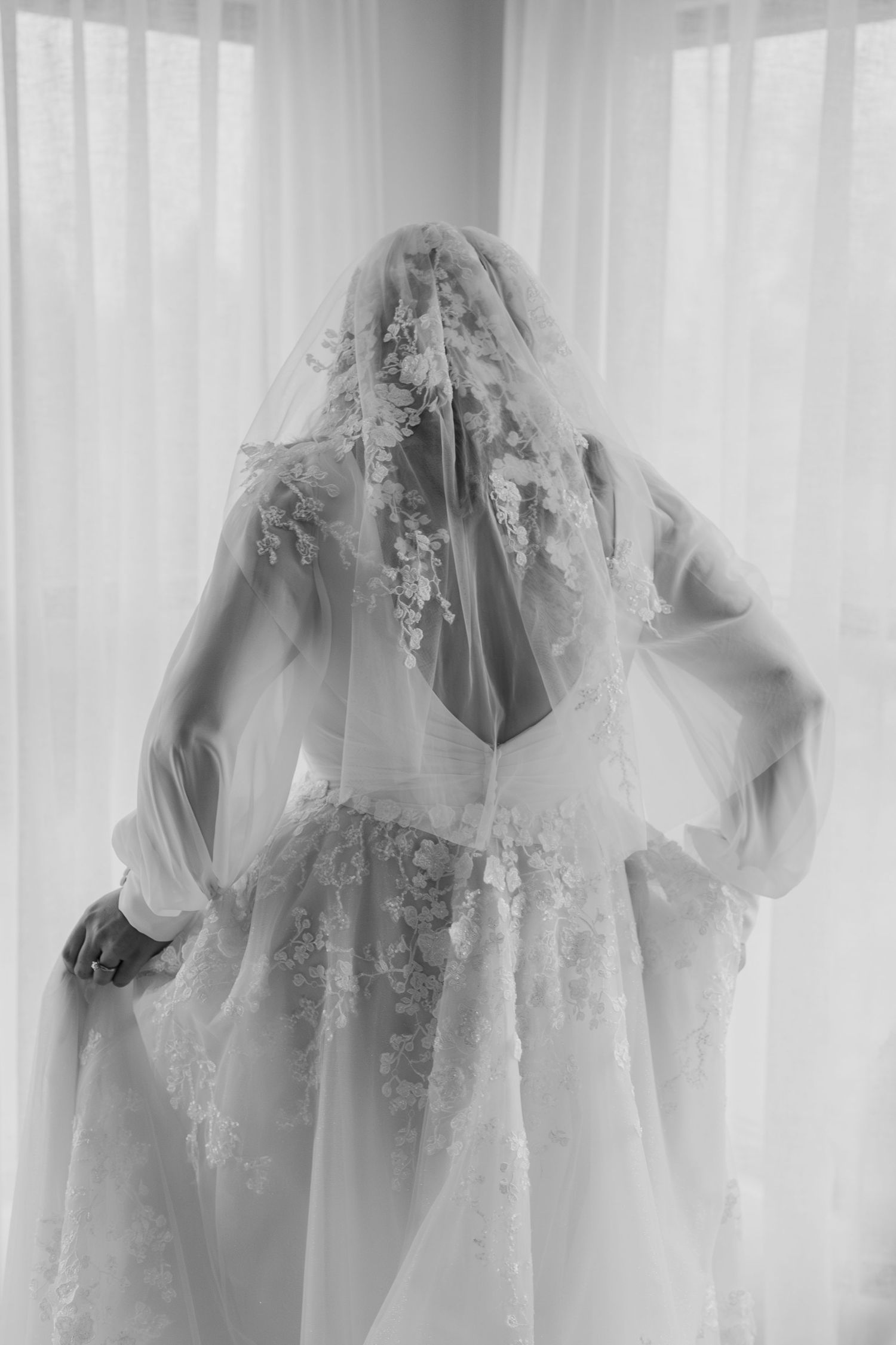 Delicate white wedding dress details with lace and tulle hanging against a light background.