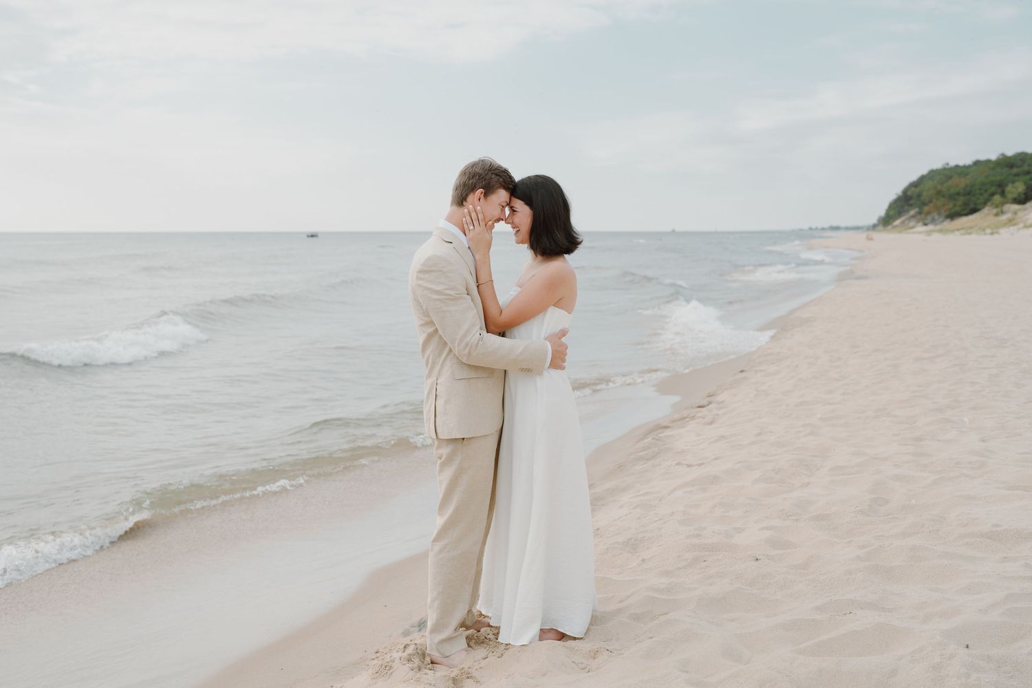 A romantic beach wedding photo of a couple embracing on the shoreline at sunset.
