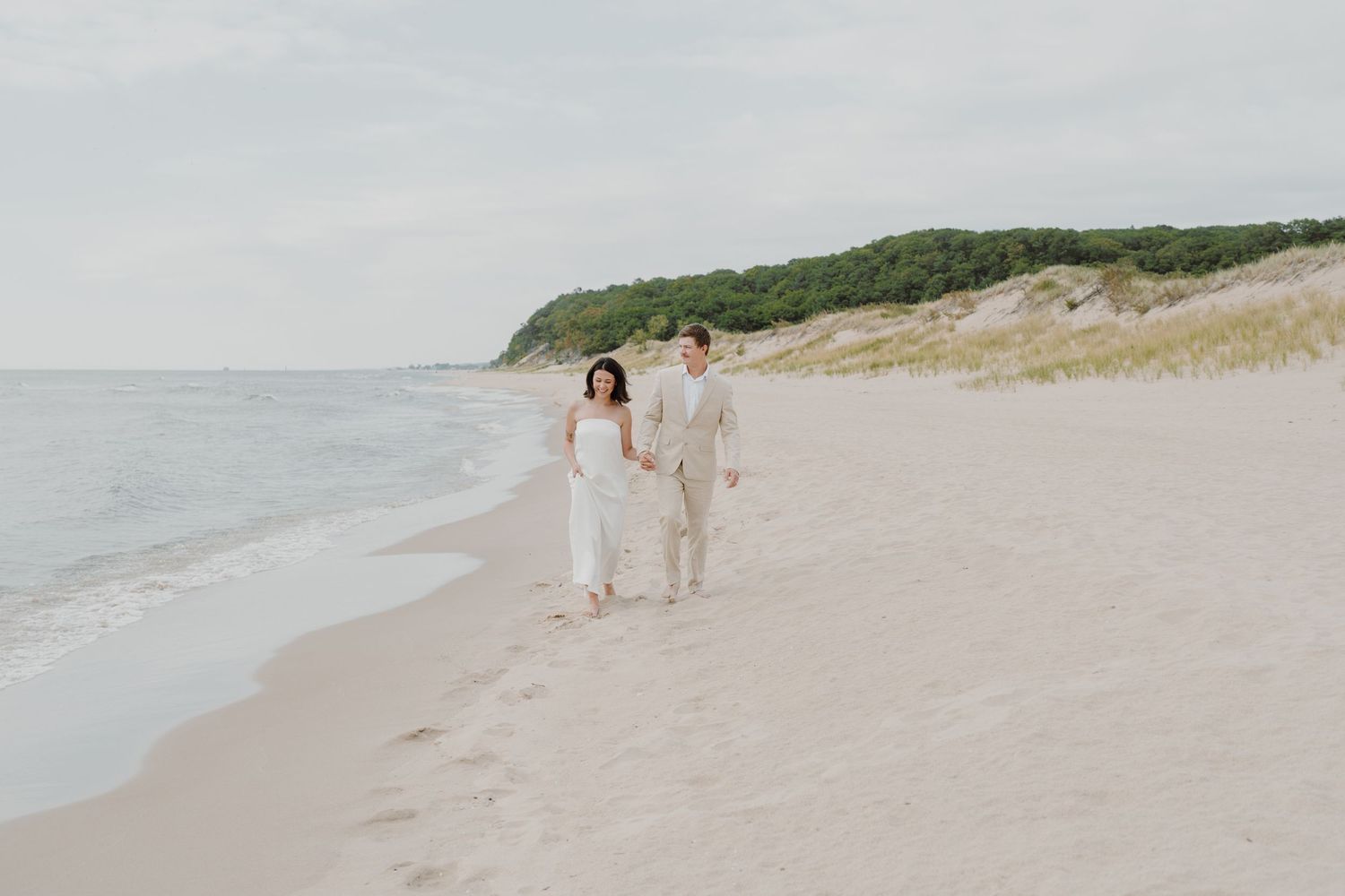 Romantic beach photoshoot featuring a couple strolling along the shoreline in light colored attire.