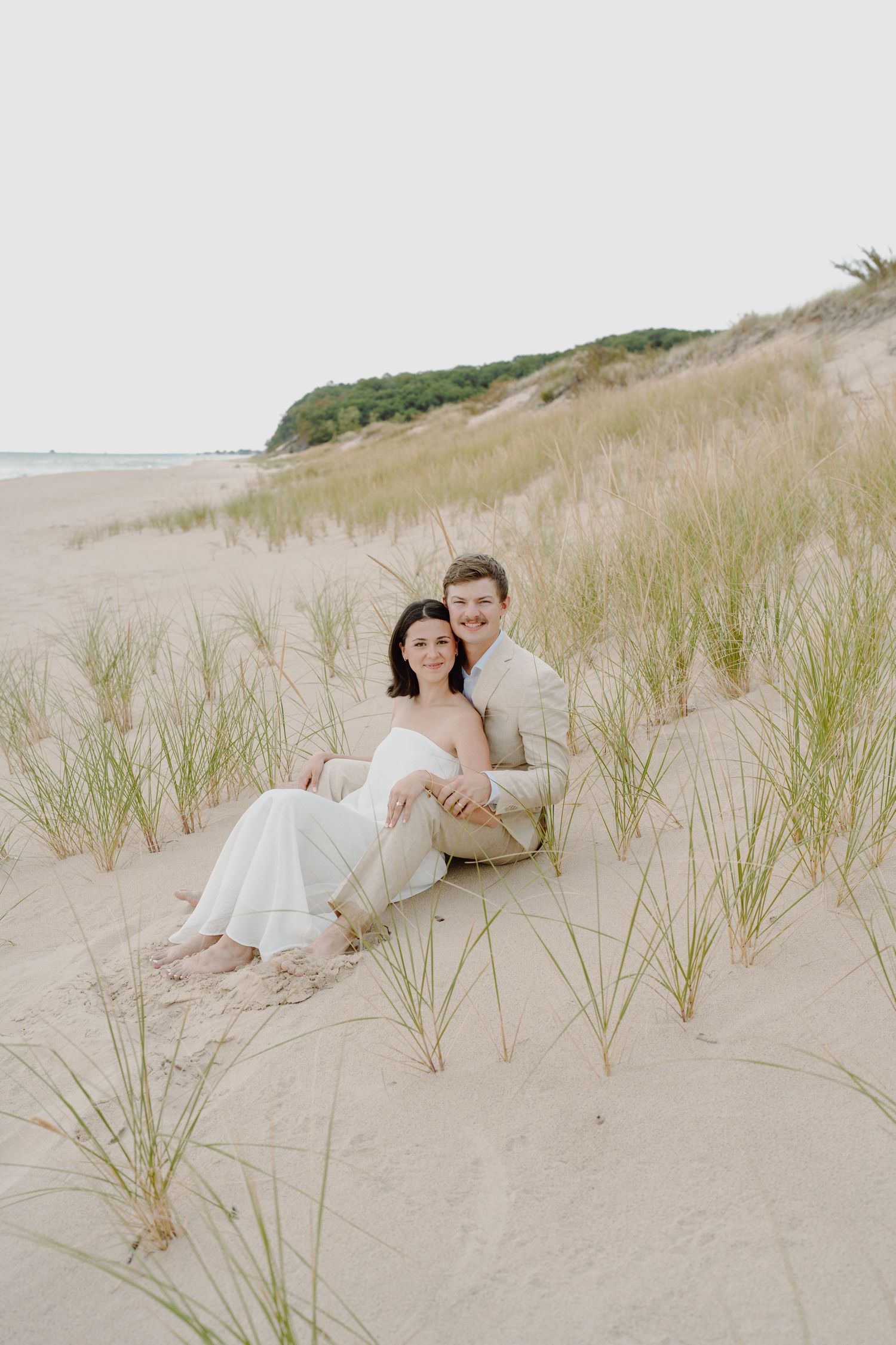 Romantic couple resting on sandy beach dunes surrounded by sea grass.
