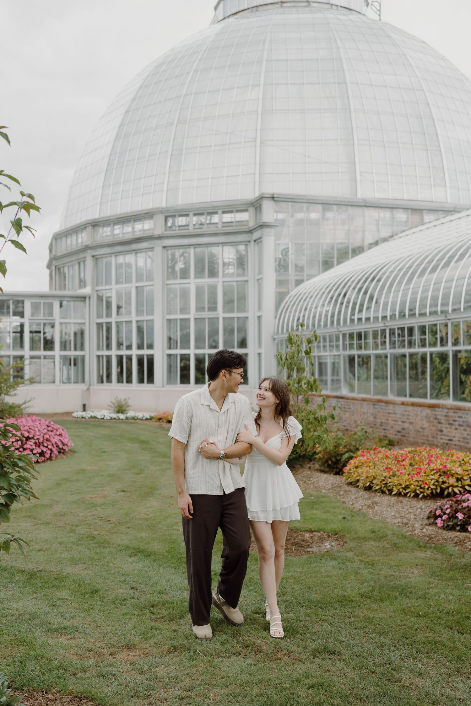A couple shares a romantic moment outside a large glass dome conservatory with flower gardens.