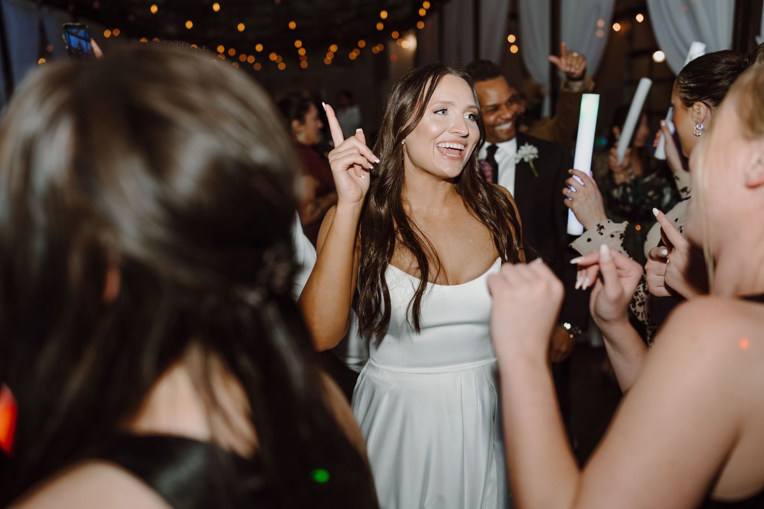 Wedding reception guests dancing and celebrating on a dimly lit dance floor with festive lighting.