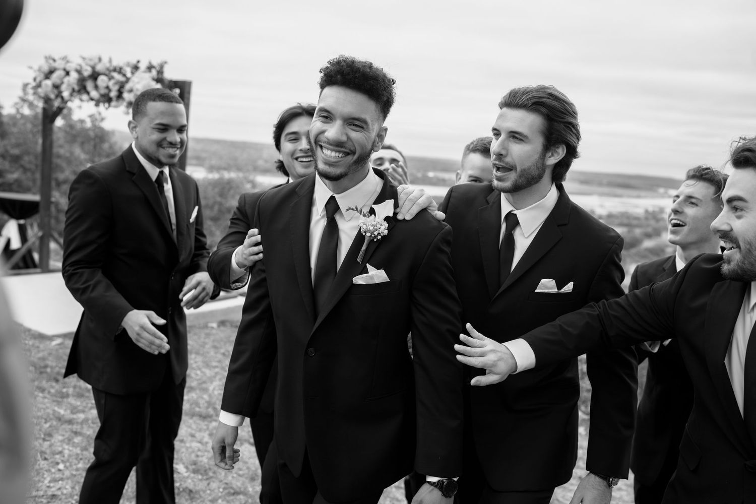 Wedding party members in black suits having fun and laughing together outdoors.