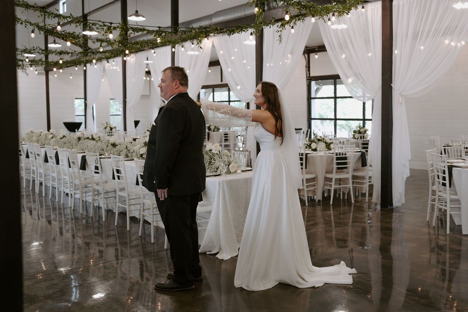 A couple shares a private first look moment in an elegant white wedding venue with draped fabric and hanging lights.