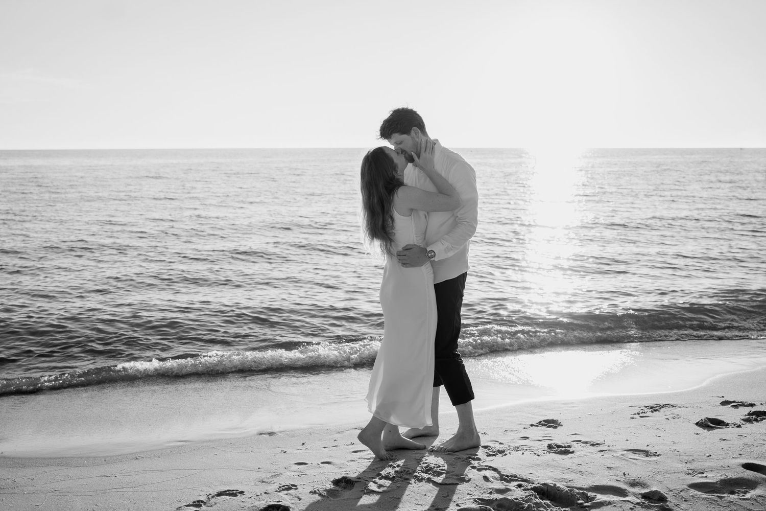 Couple embracing on sandy beach during sunset photoshoot.