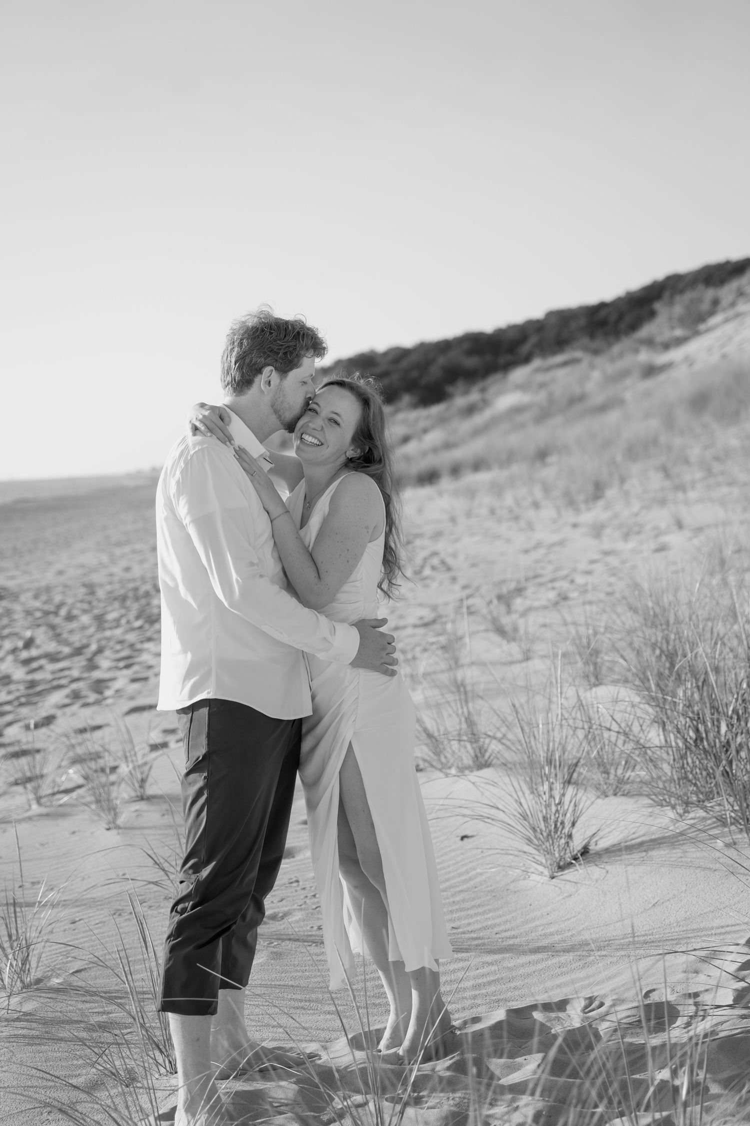 Black and white photo of an intimate embrace on a scenic beach landscape.