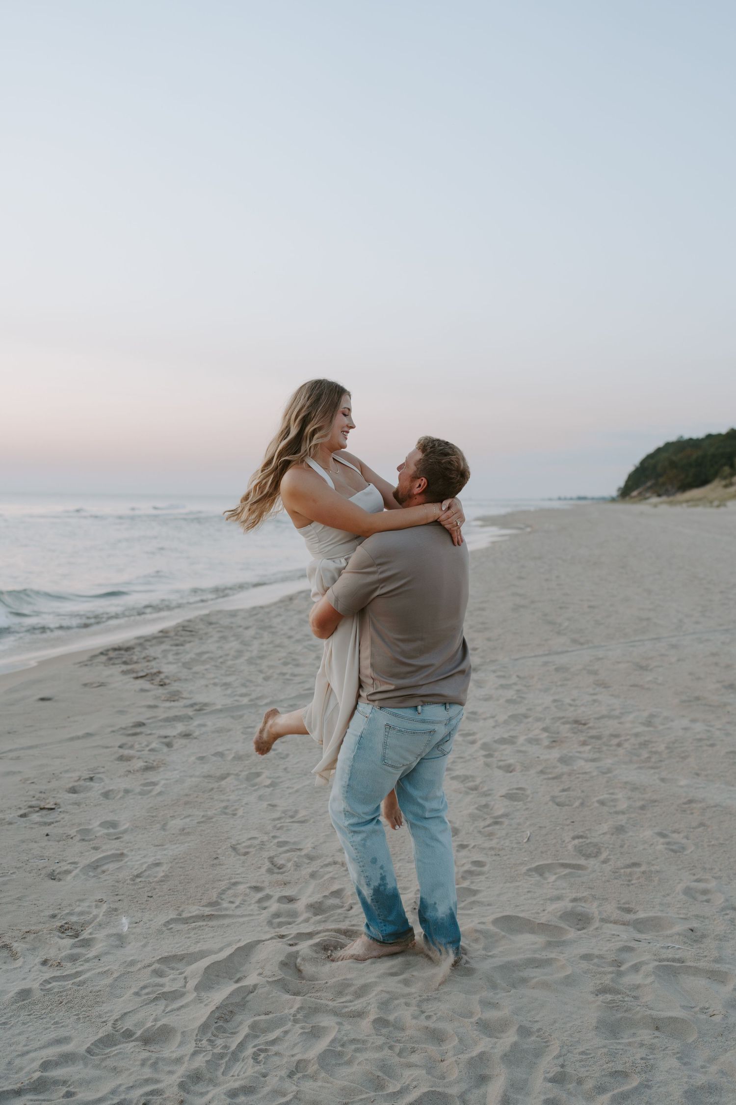 A couple plays and laughs together during their beach engagement photoshoot at dusk.