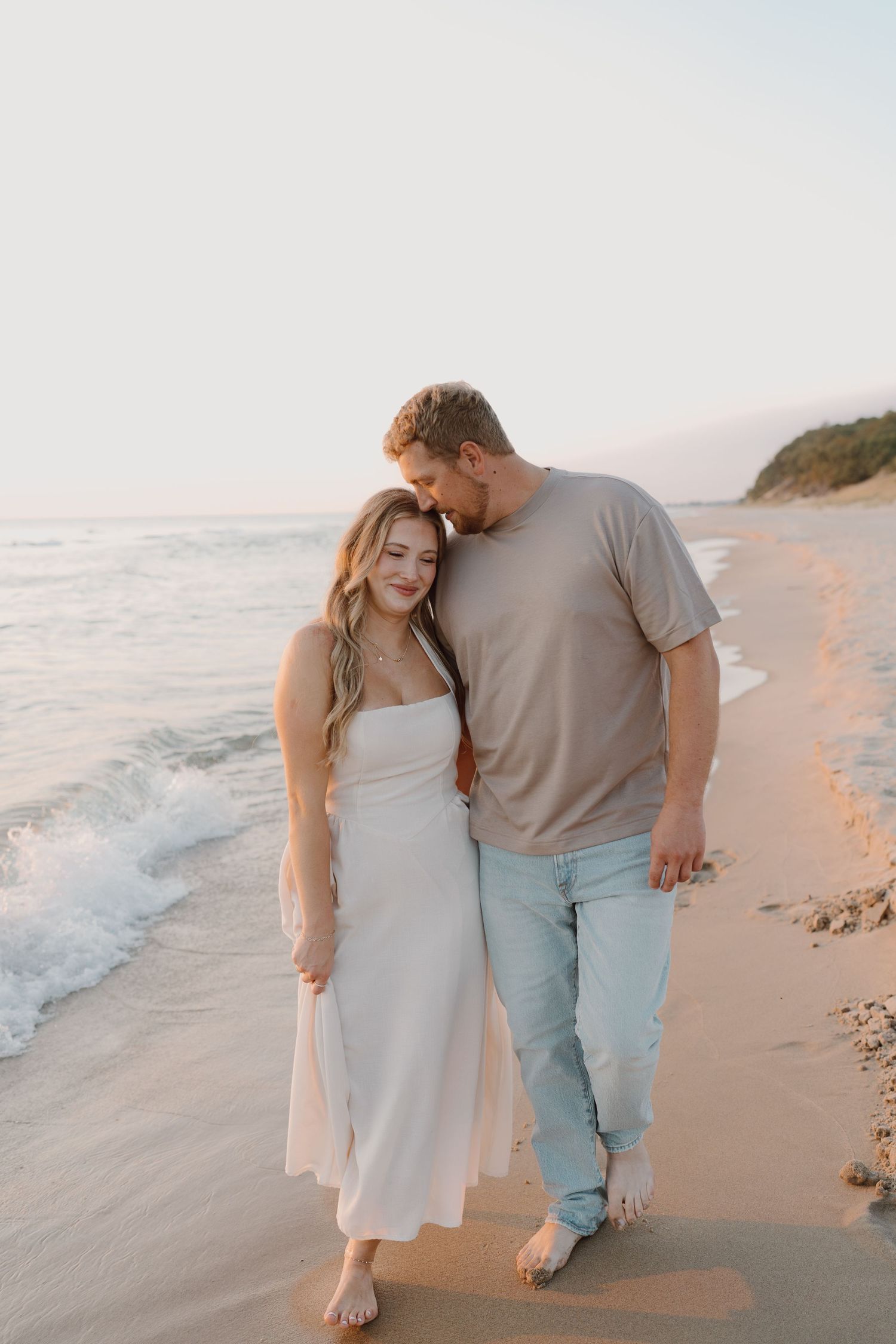 A tender moment between two people walking on a quiet beach with soft sunset lighting.