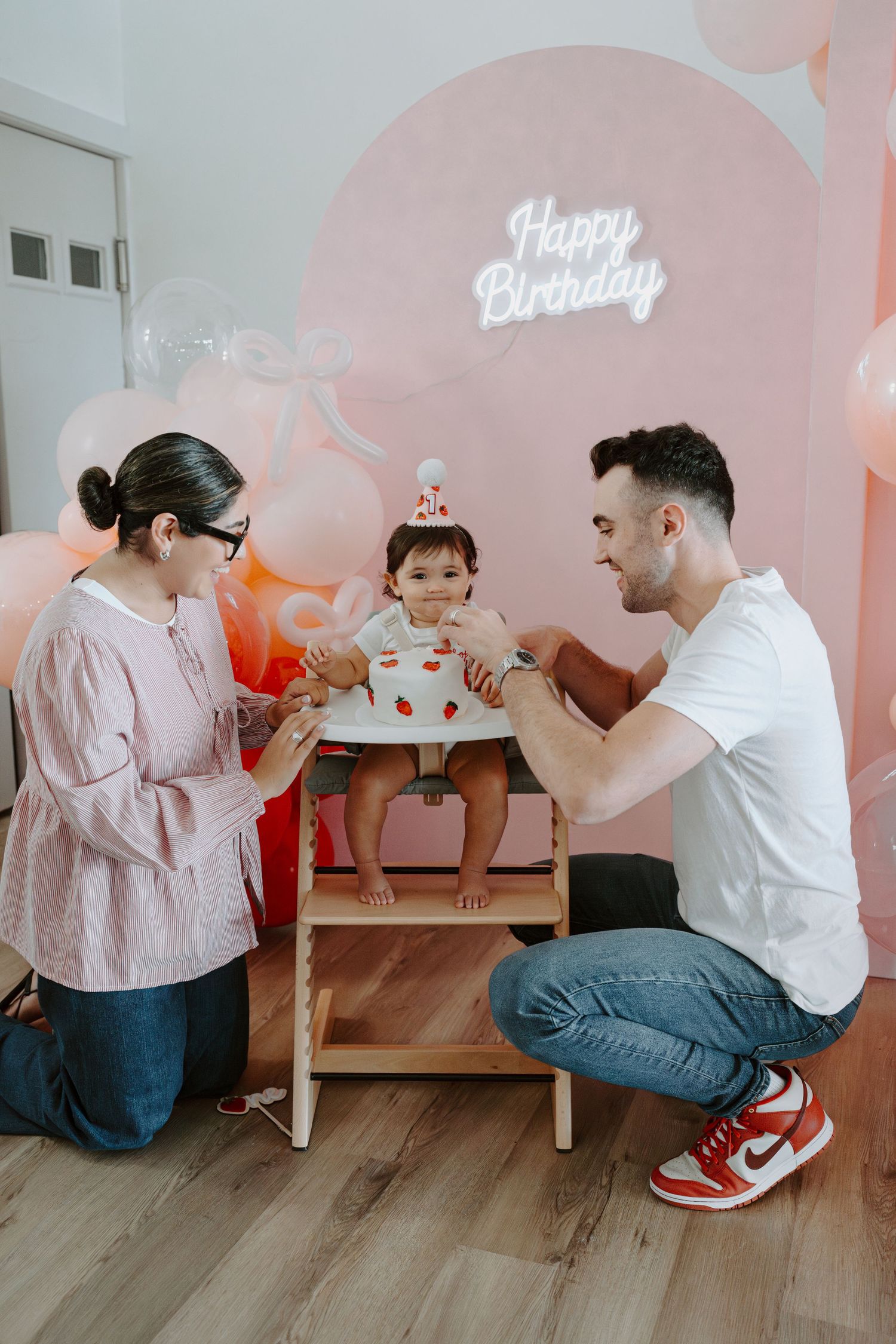 A birthday celebration setup with pink balloons and neon sign against a light colored wall.