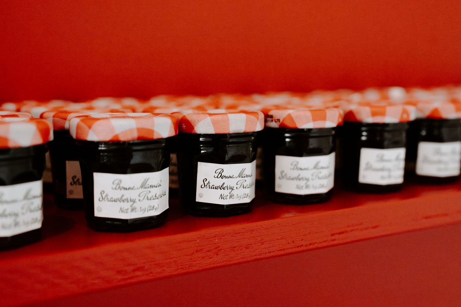 Row of small black jars with labels arranged on red surface.