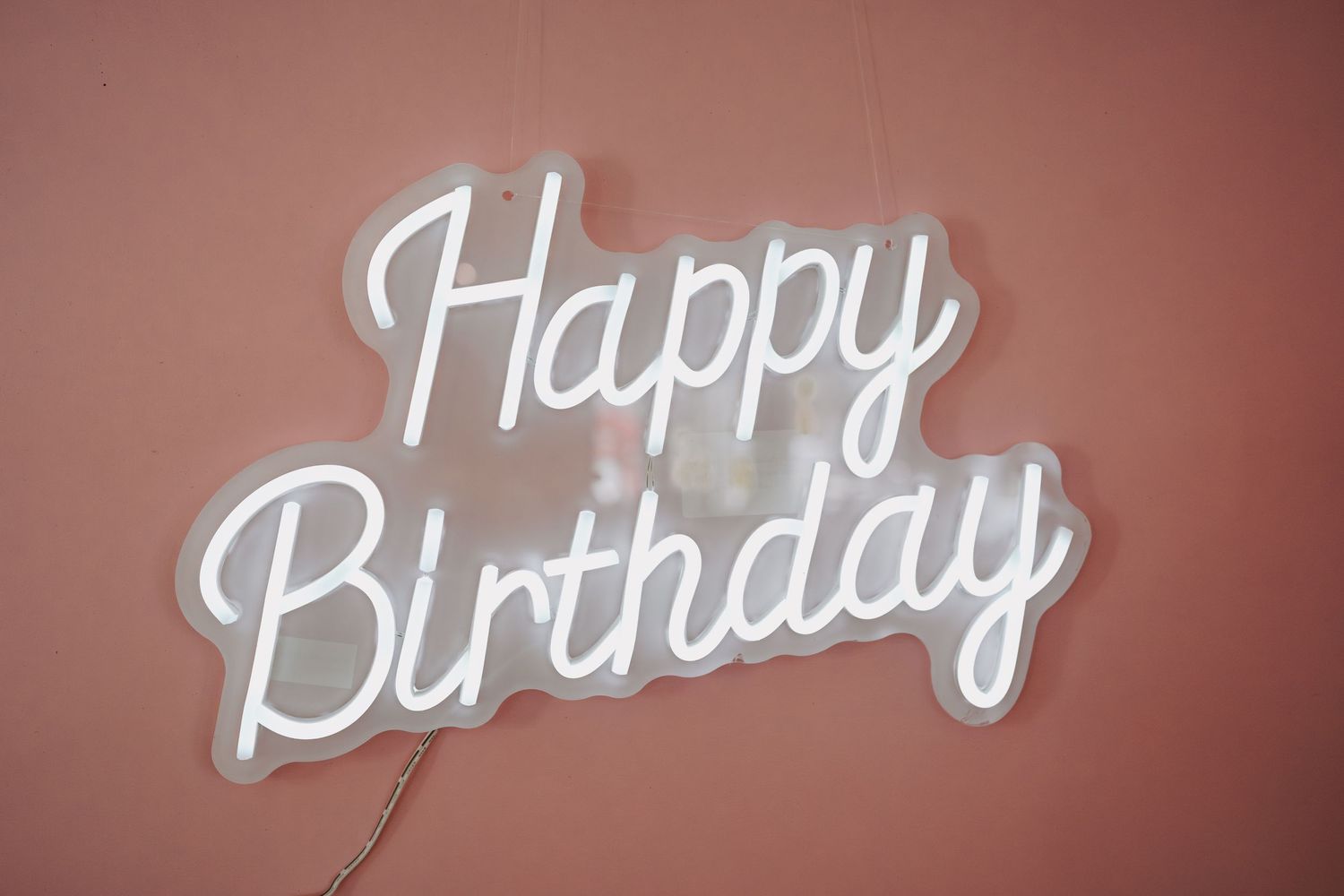 Cursive white 'Happy Birthday' lettering displayed on a salmon-colored wall.