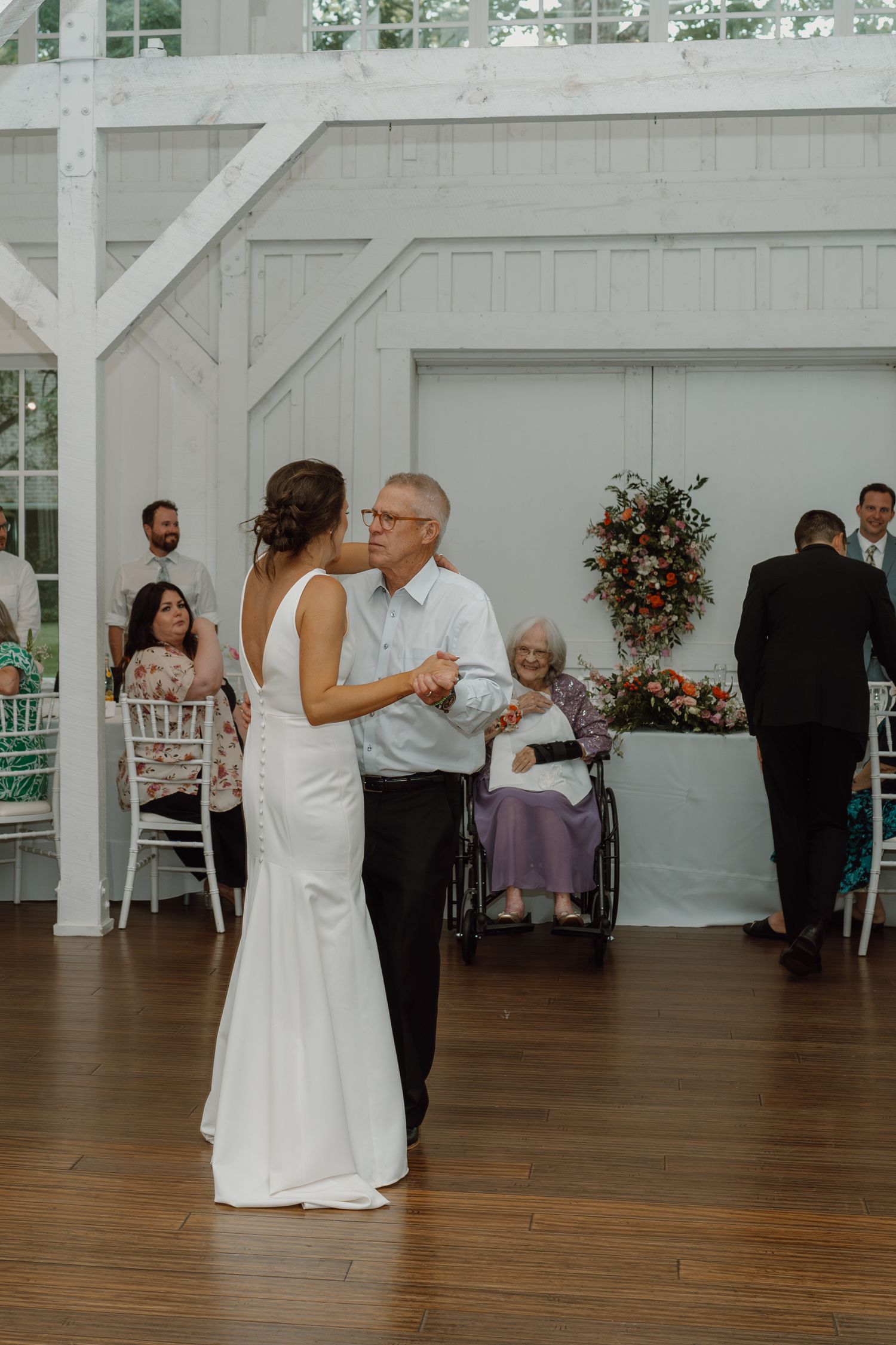 Wedding celebration in progress at a bright white barn venue with dancing and seated guests.