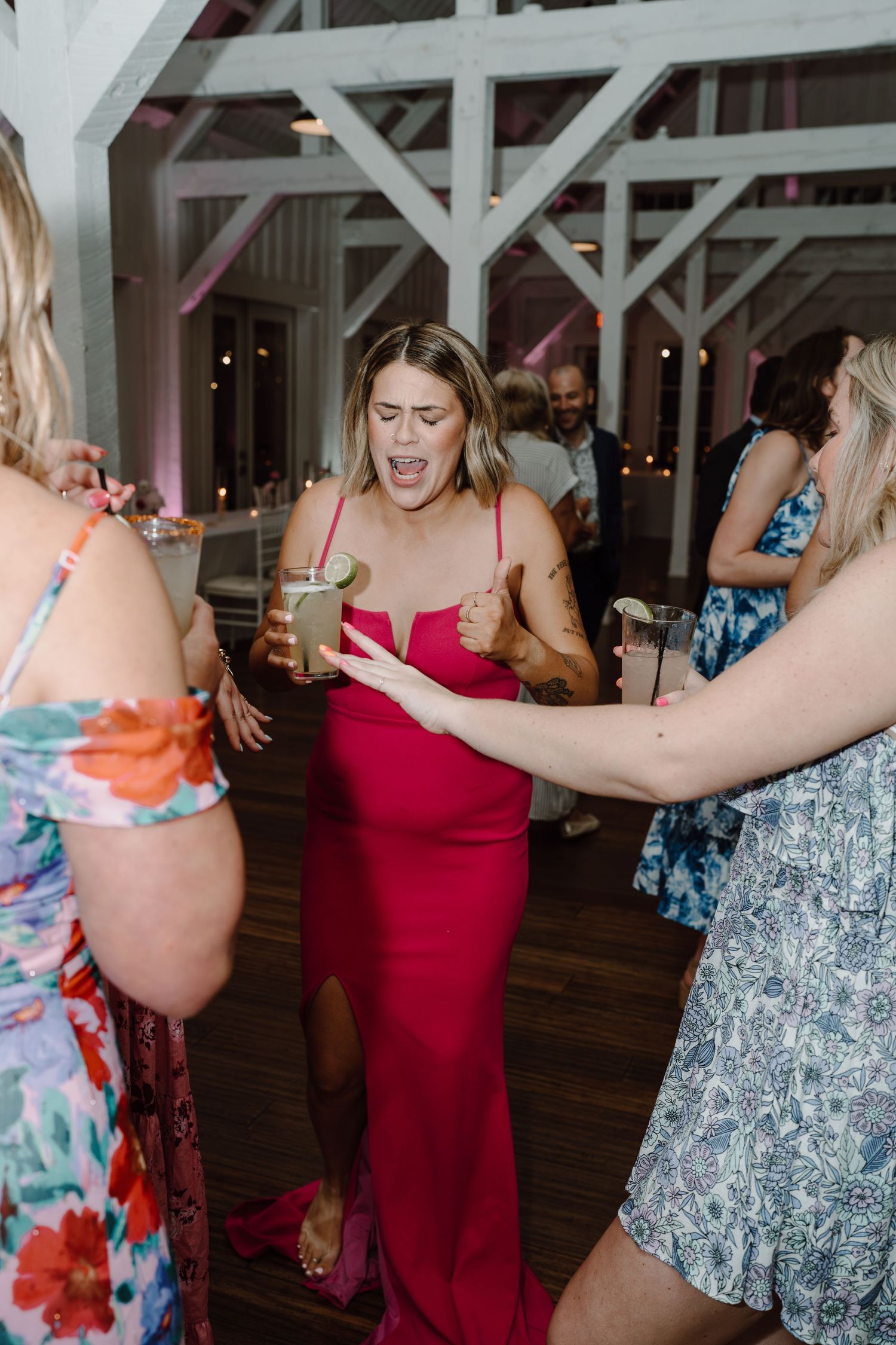 Wedding guests in bright dresses dance and celebrate on a wooden dance floor.