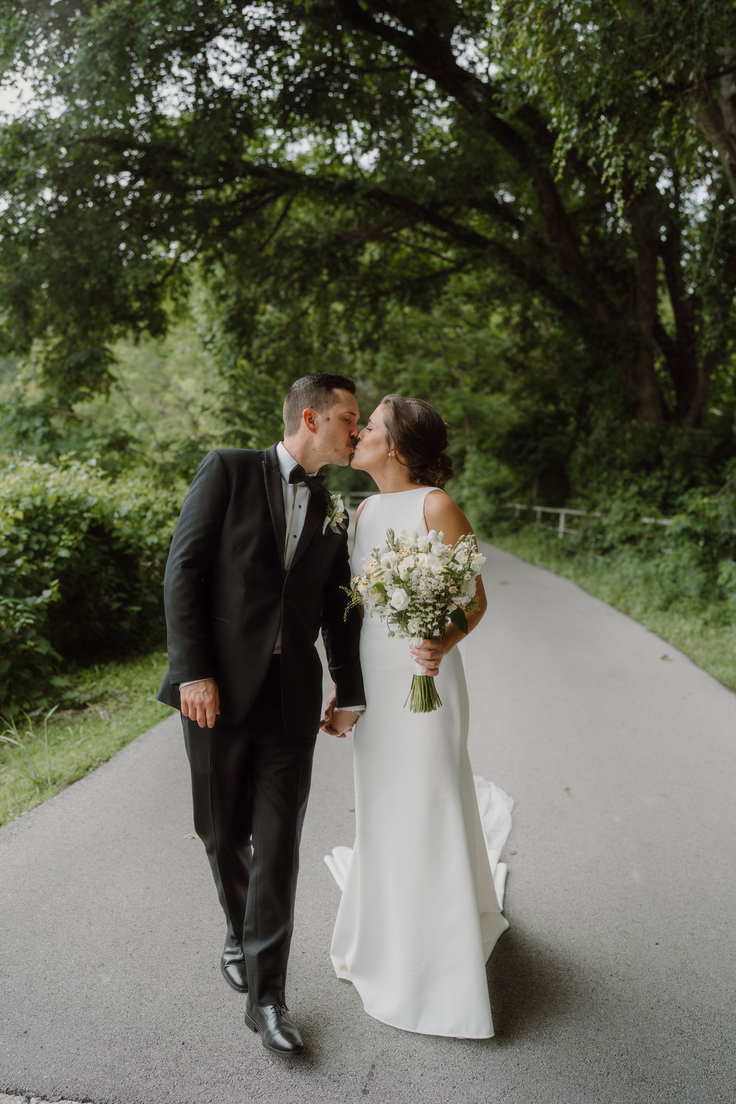 Wedding couple shares an intimate moment on a tree-lined path during their special day.