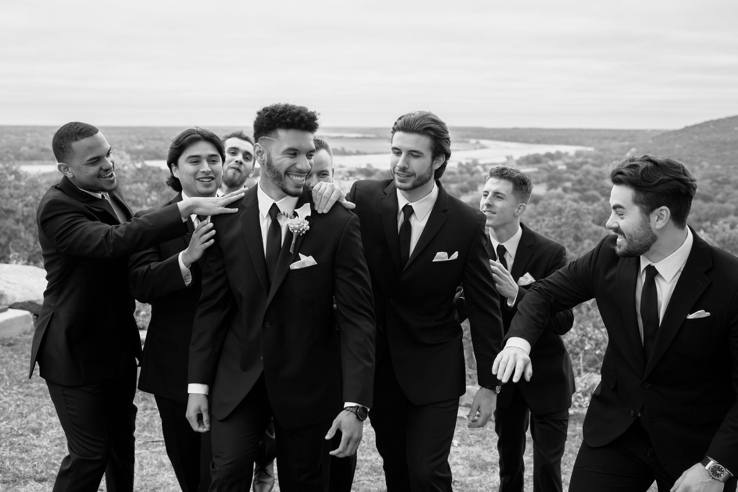 Wedding party members in formal attire enjoying candid moments together on a hilltop.
