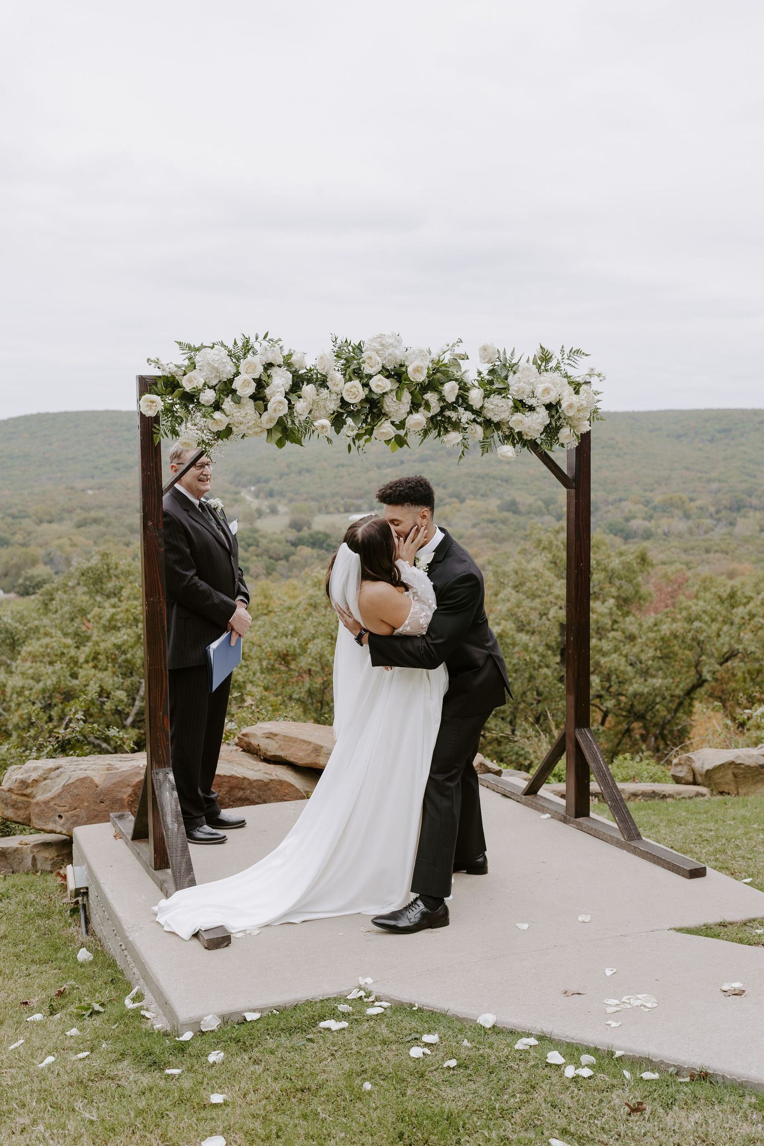 Wedding ceremony on stone platform with wooden arch and mountain views.