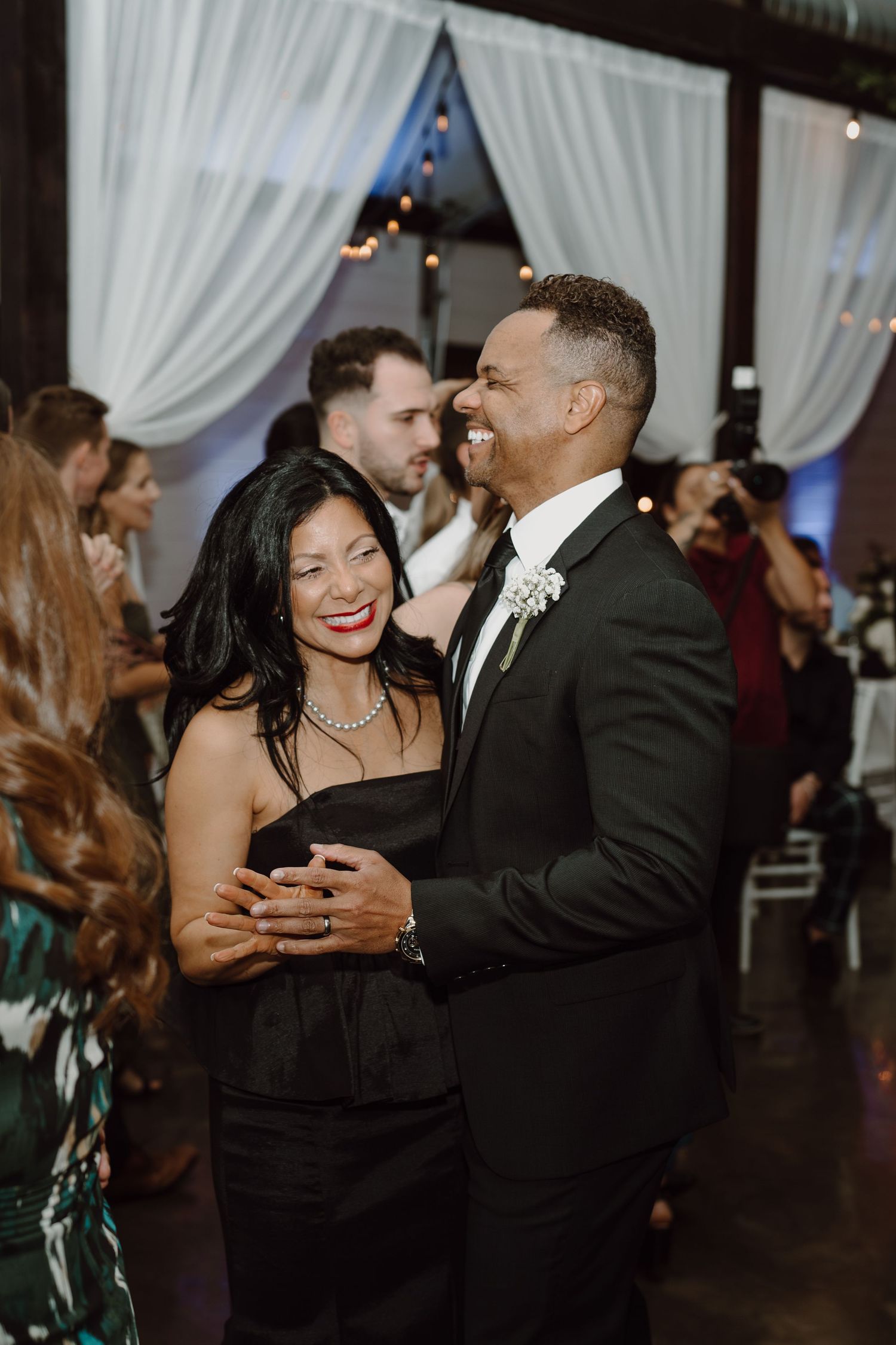 Couple sharing an intimate moment while dancing at a wedding reception with white drapes and soft lighting.