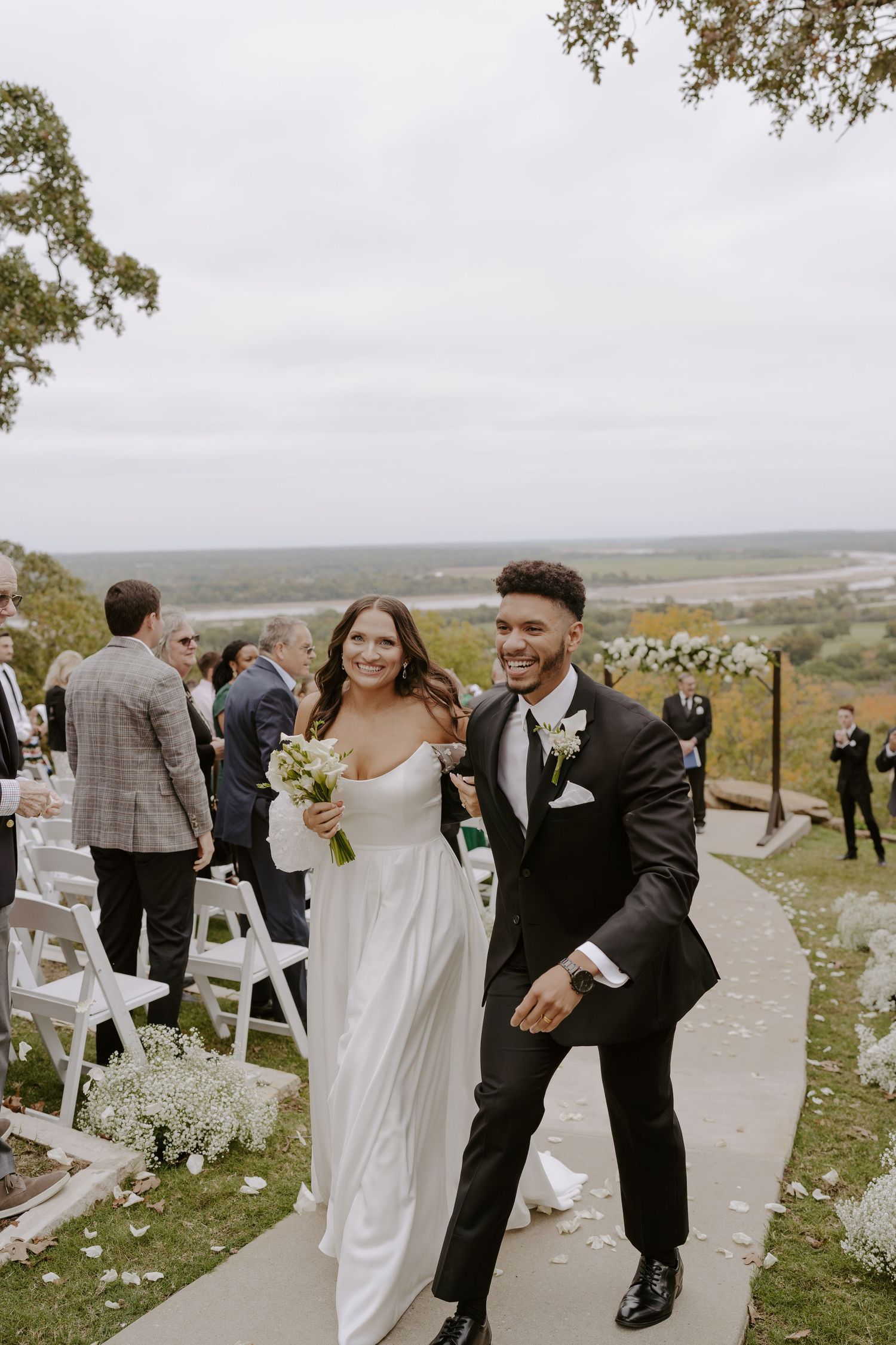 A joyful newlywed couple walks down the aisle at their outdoor hillside wedding ceremony.
