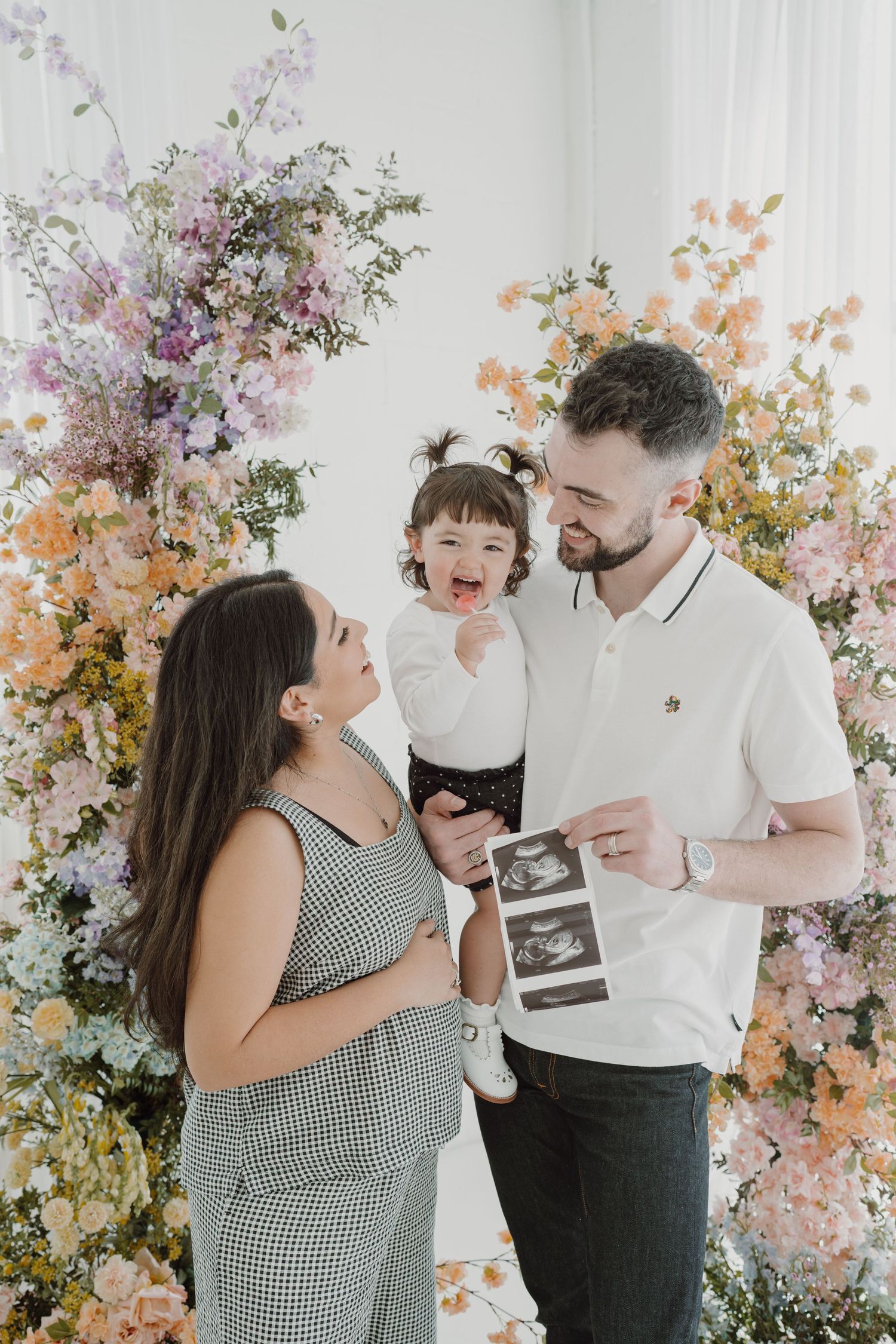 Family shares happy moment during pregnancy announcement photoshoot with floral decorations.