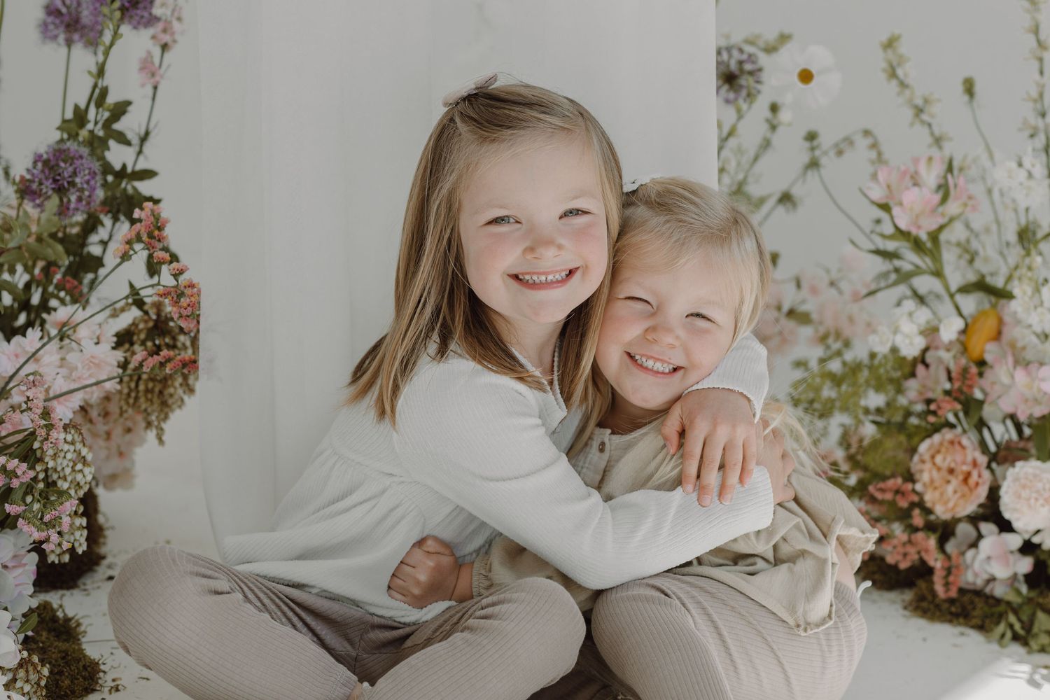Two people share joyful moments in a bright white studio setting with delicate floral arrangements.