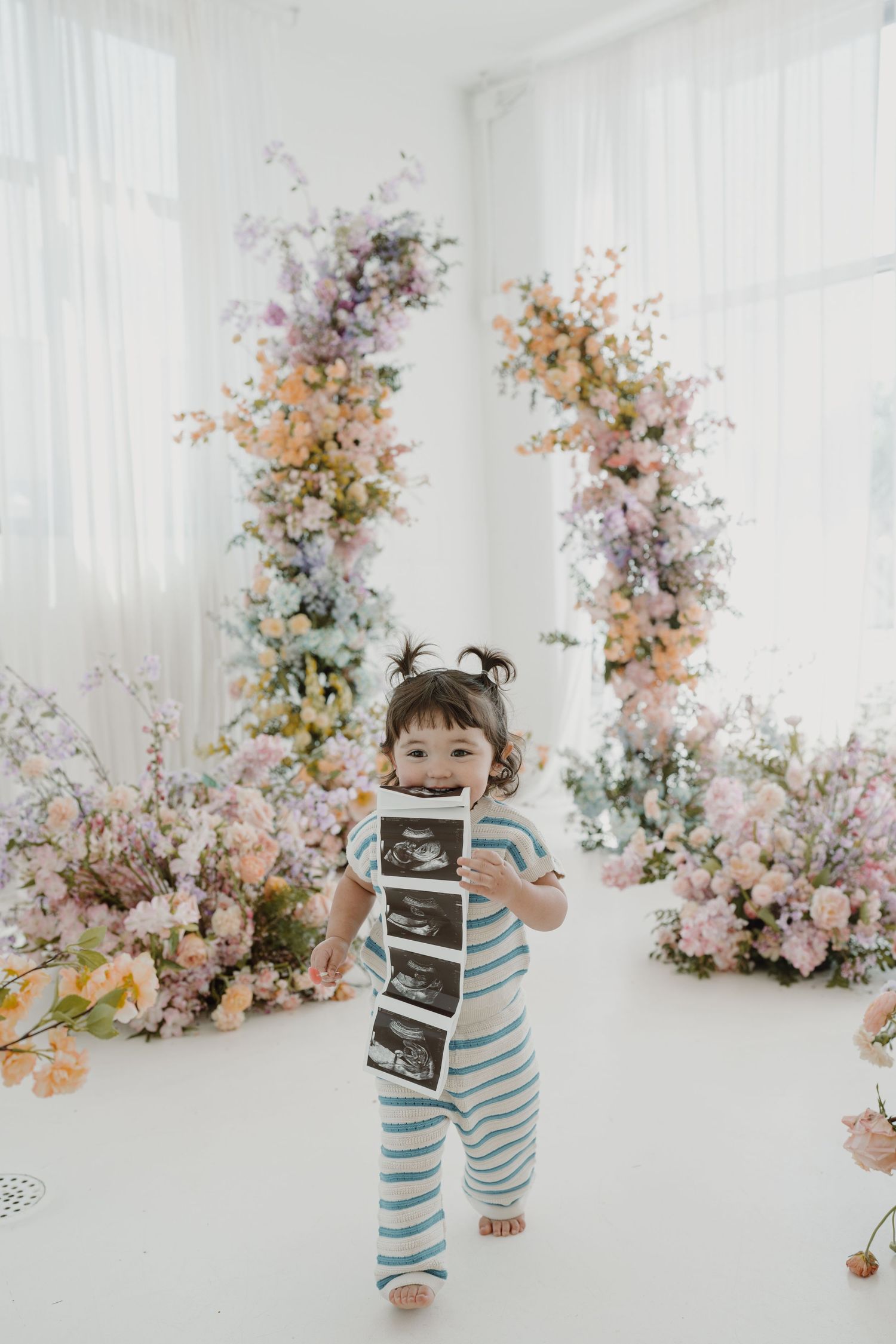 Candid moment in white studio with blue striped outfit and ultrasound photos.