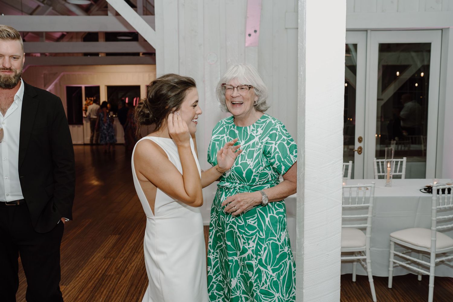 Wedding guests dance and celebrate together in a rustic barn venue with white beams and wooden floors.